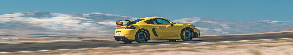A yellow sports car racing on a road with mountains in the background.