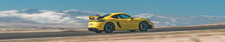 A yellow sports car racing on a road with mountains in the background.