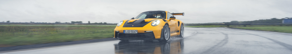 A yellow Porsche racing car driving on a wet, rainy track.