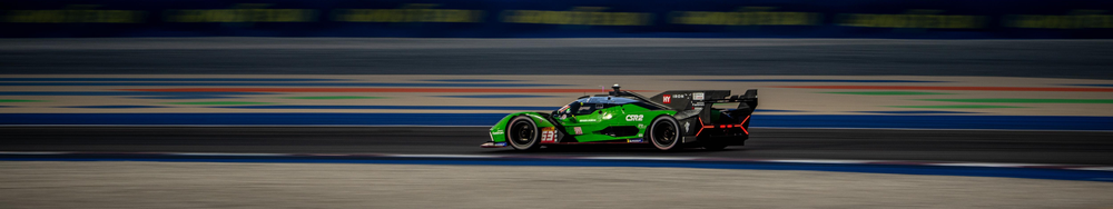 Green race car speeding on a race track with blurred colorful lines in the background.