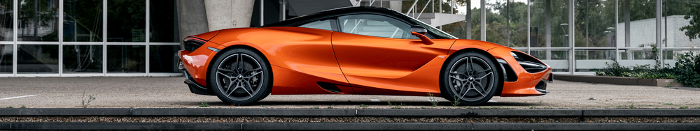 An orange sports car parked outdoors on a concrete surface in front of a modern building with large glass windows.