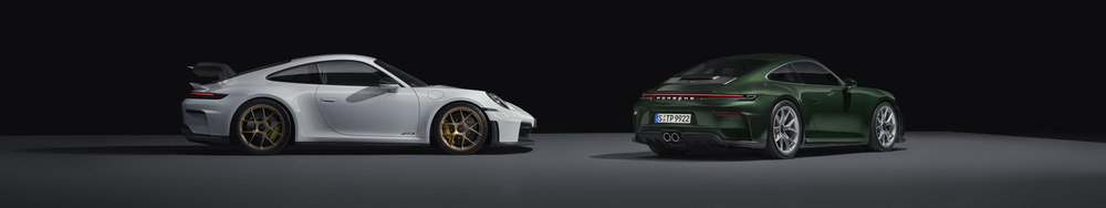 Two modern sports cars, a white Porsche 911 GT3 and a green Porsche 911, parked side by side in a dark space with minimal lighting.