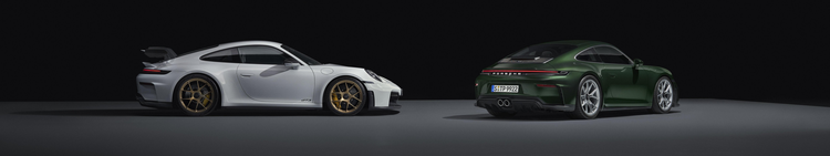 Two modern sports cars, a white Porsche 911 GT3 and a green Porsche 911, parked side by side in a dark space with minimal lighting.