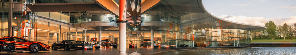Modern car showroom with luxury sports cars displayed indoors and large glass windows showing a grassy outdoor area, during sunset.
