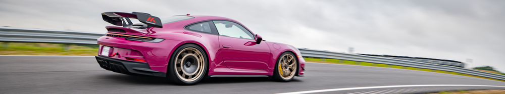 Pink sports car on a racetrack with a gray sky in the background.