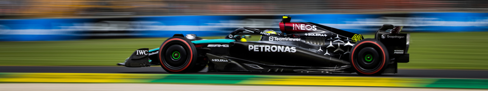 F1 race car on a track with sponsorship logos, moving at high speed with blurred background.