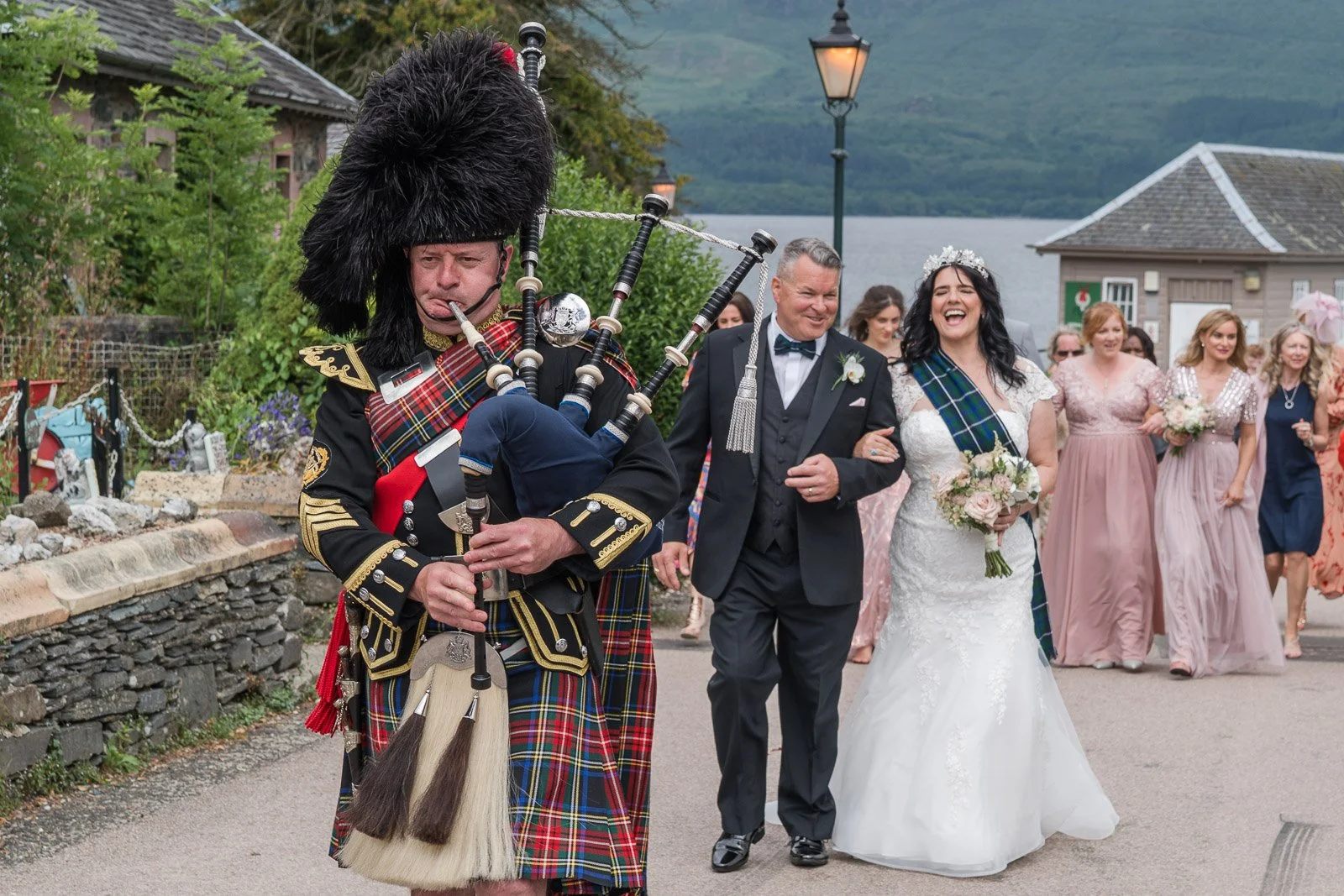 Newly married couple walking through Luss, Loch Lomond with a piper