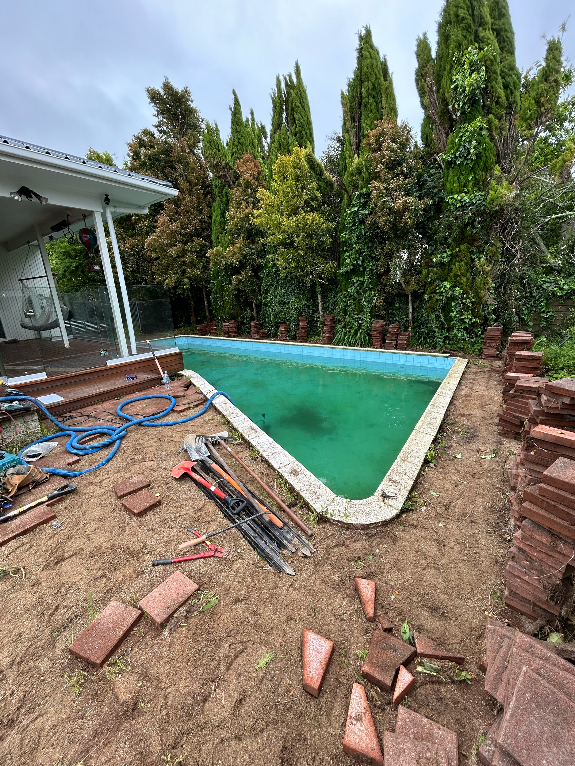 Backyard with a rectangular in-ground swimming pool, part of pool refurbishment build Auckland. With a deck and glass railing. Built by ESC outdoor living swimming pool builders. Auckland.