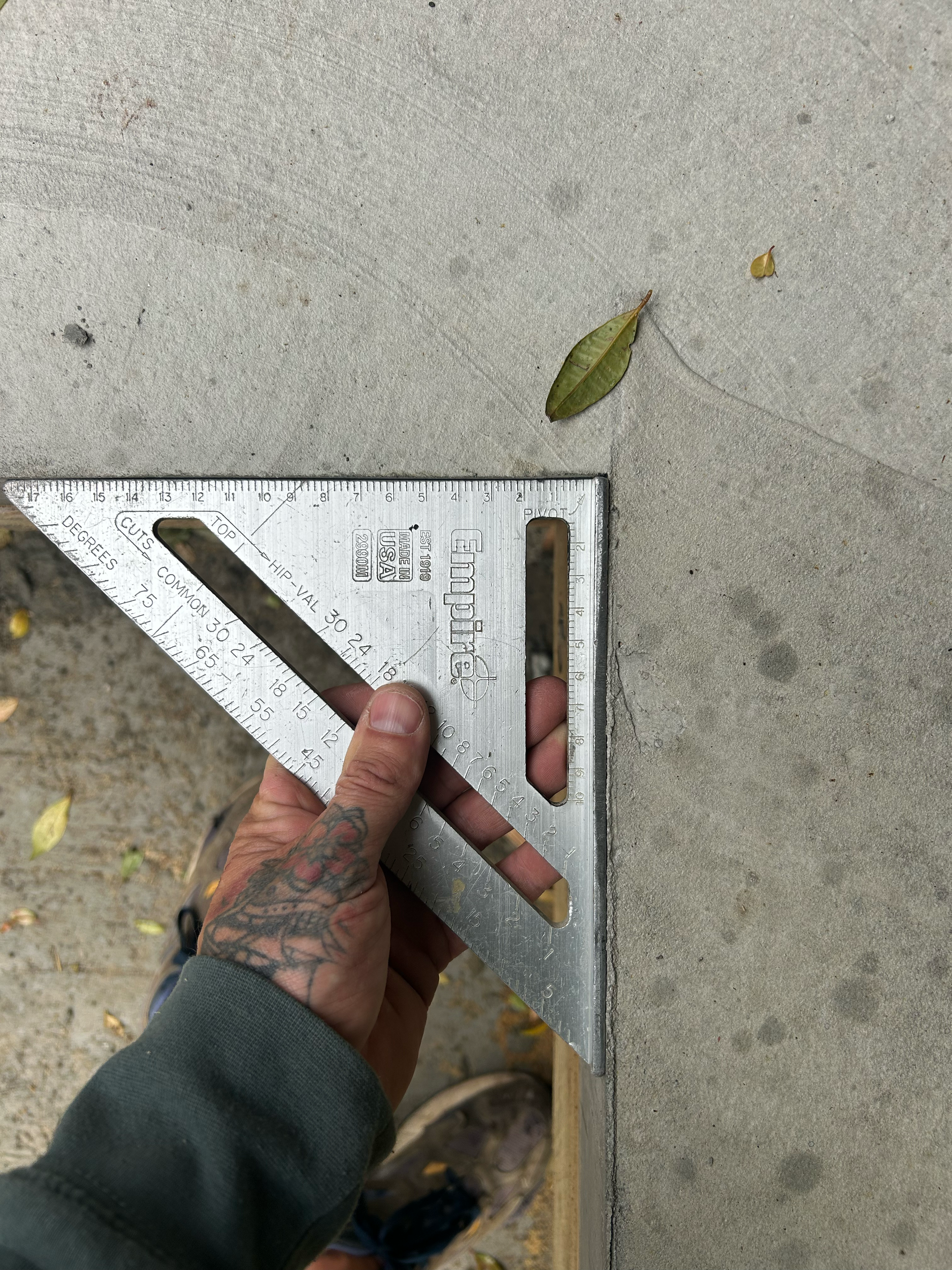 A person's hand holding a metal square ruler against a concrete surface, with leaves nearby. Existing pool refurbishment Built by ESC outdoor living swimming pool builders. Auckland. skilled builders