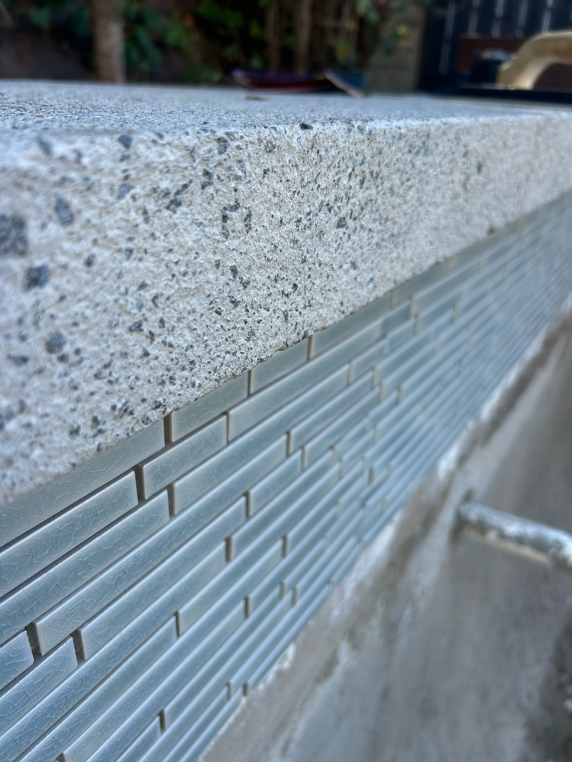 Close-up of a concrete swimming pool with a textured, speckled surface next to a tiled wall with small, rectangular, light blue tiles. Existing pool refurbishment Built by ESC outdoor living swimming pool builders. Auckland. skilled builders