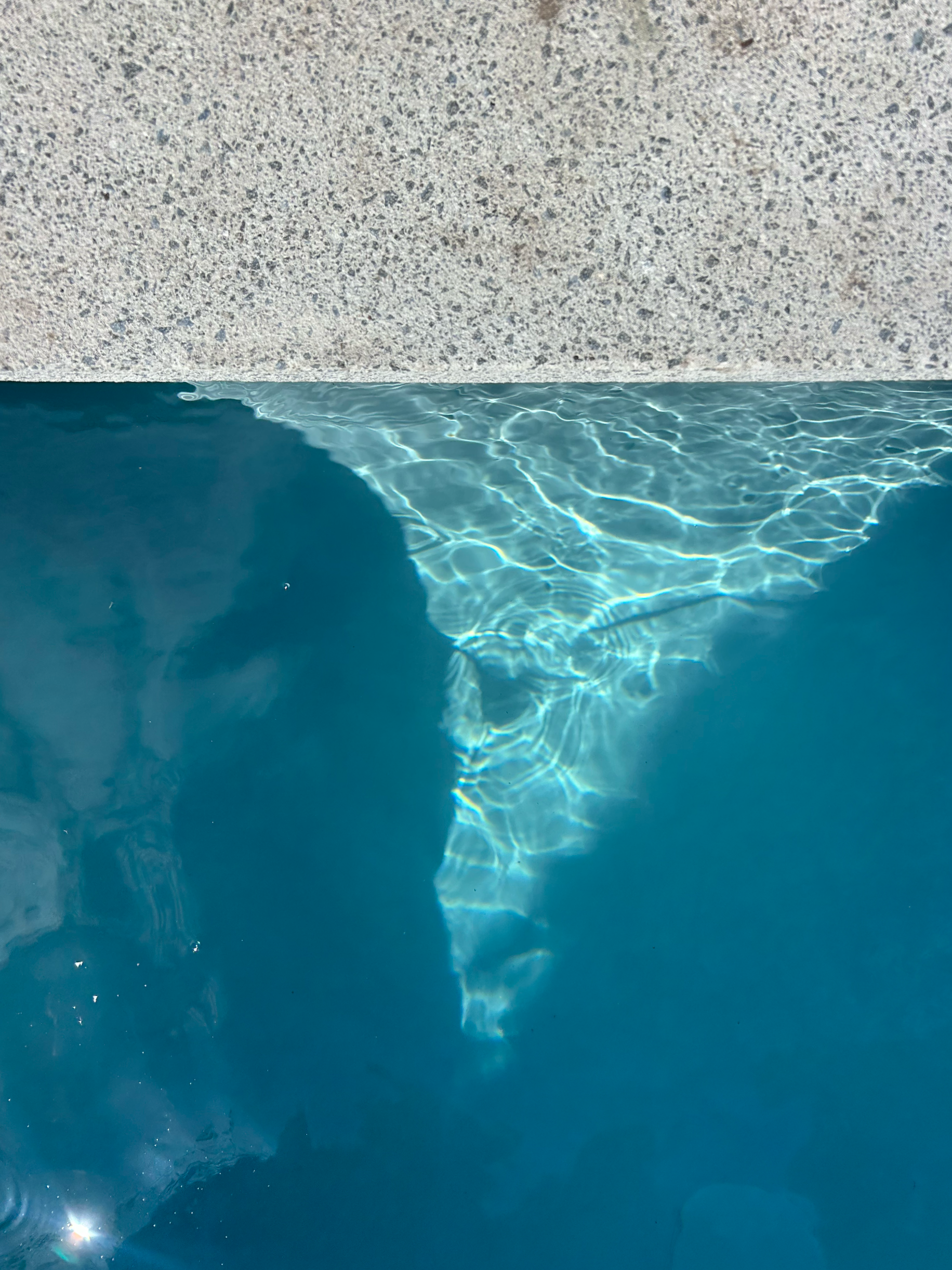 Close-up of a swimming pool with clear blue water and a beige textured poolside edge. Existing pool refurbishment Built by ESC outdoor living swimming pool builders. Auckland. skilled builders