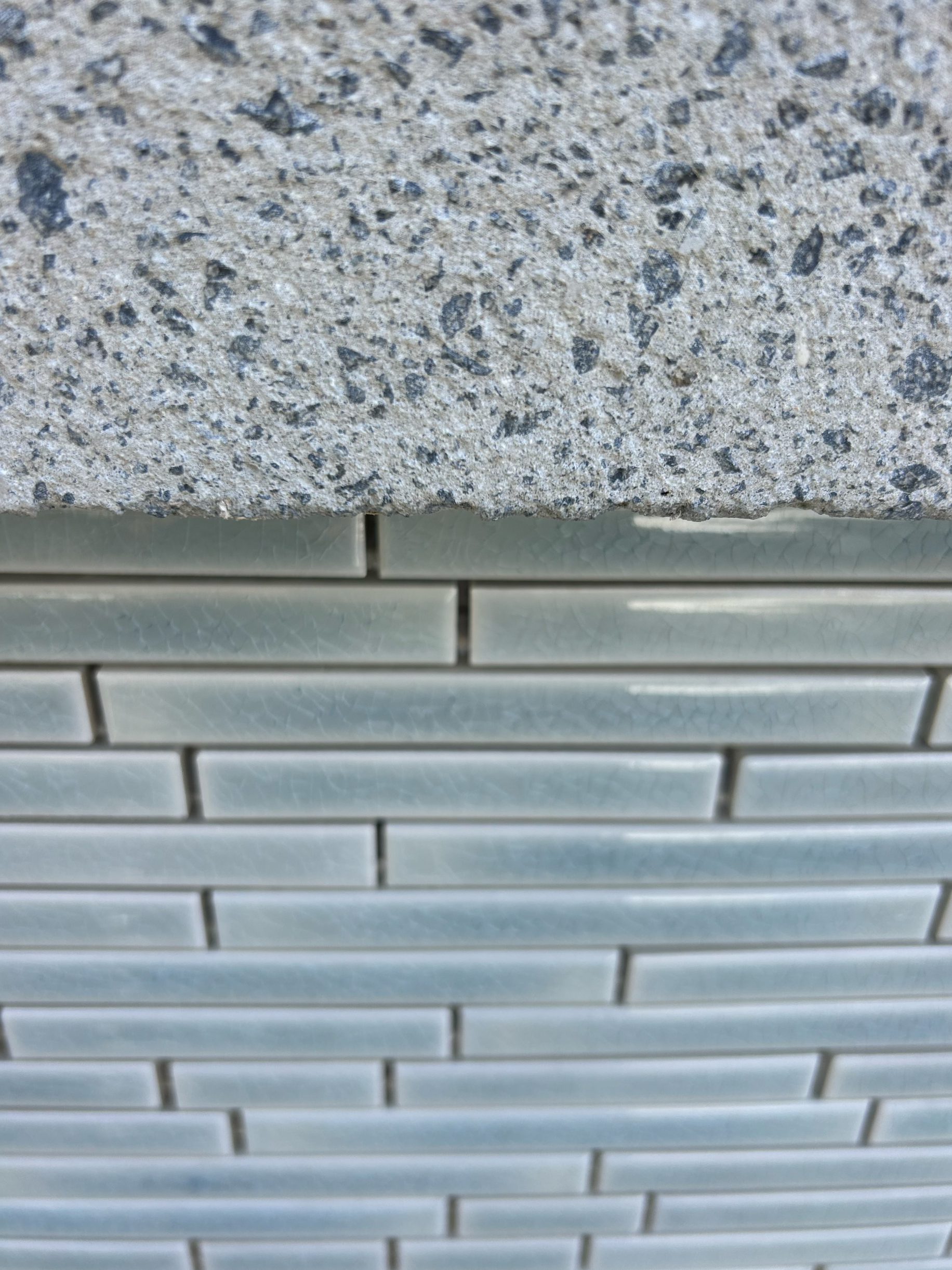 Close-up of a textured concrete top and a tiled wall below with horizontal, elongated, off-white tiles. Existing pool refurbishment Built by ESC outdoor living swimming pool builders. Auckland. skilled builders