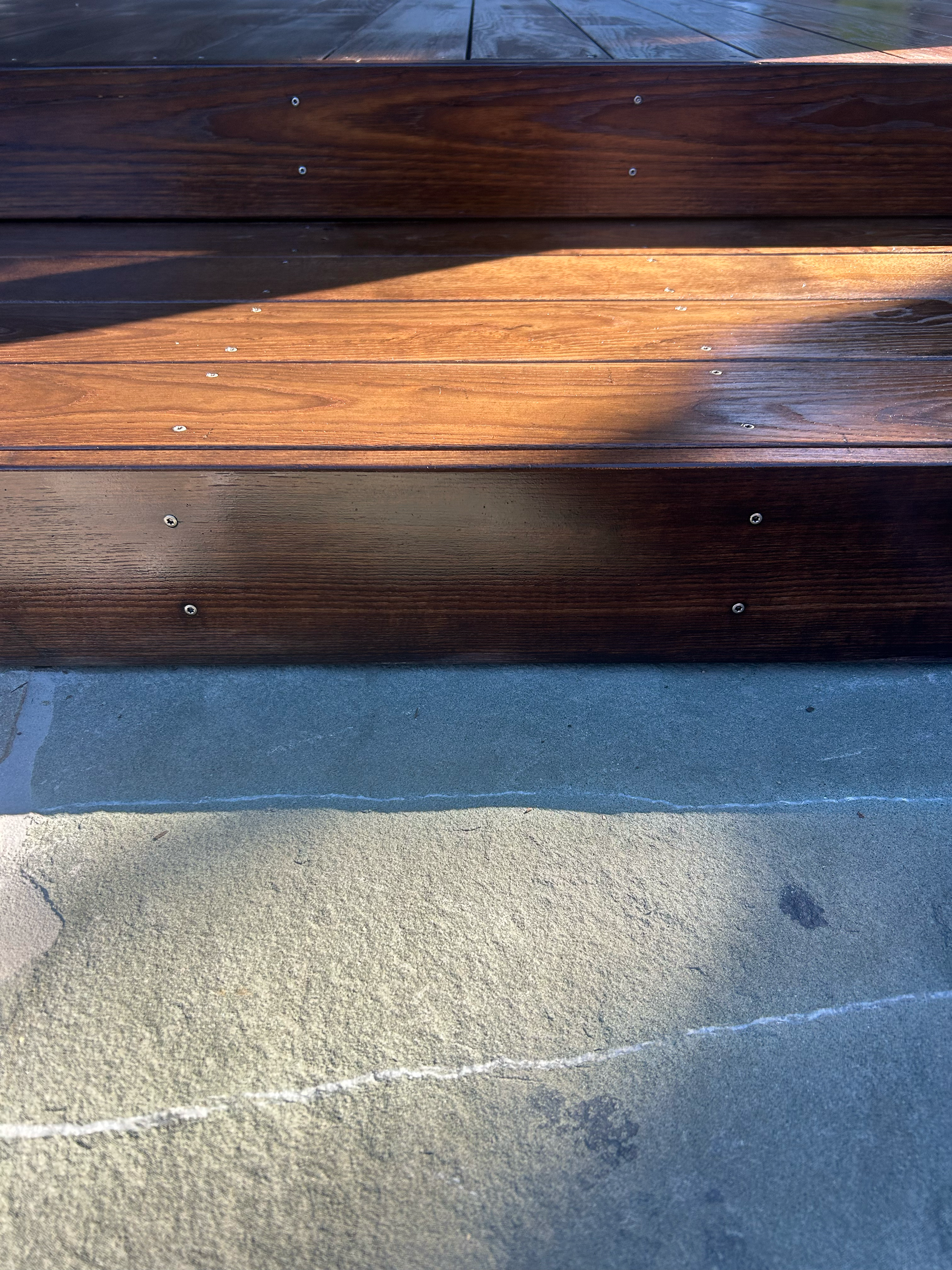 Close-up of wooden stairs with shadow and concrete ground underneath. Existing pool refurbishment Built by ESC outdoor living swimming pool builders. Auckland. skilled builders