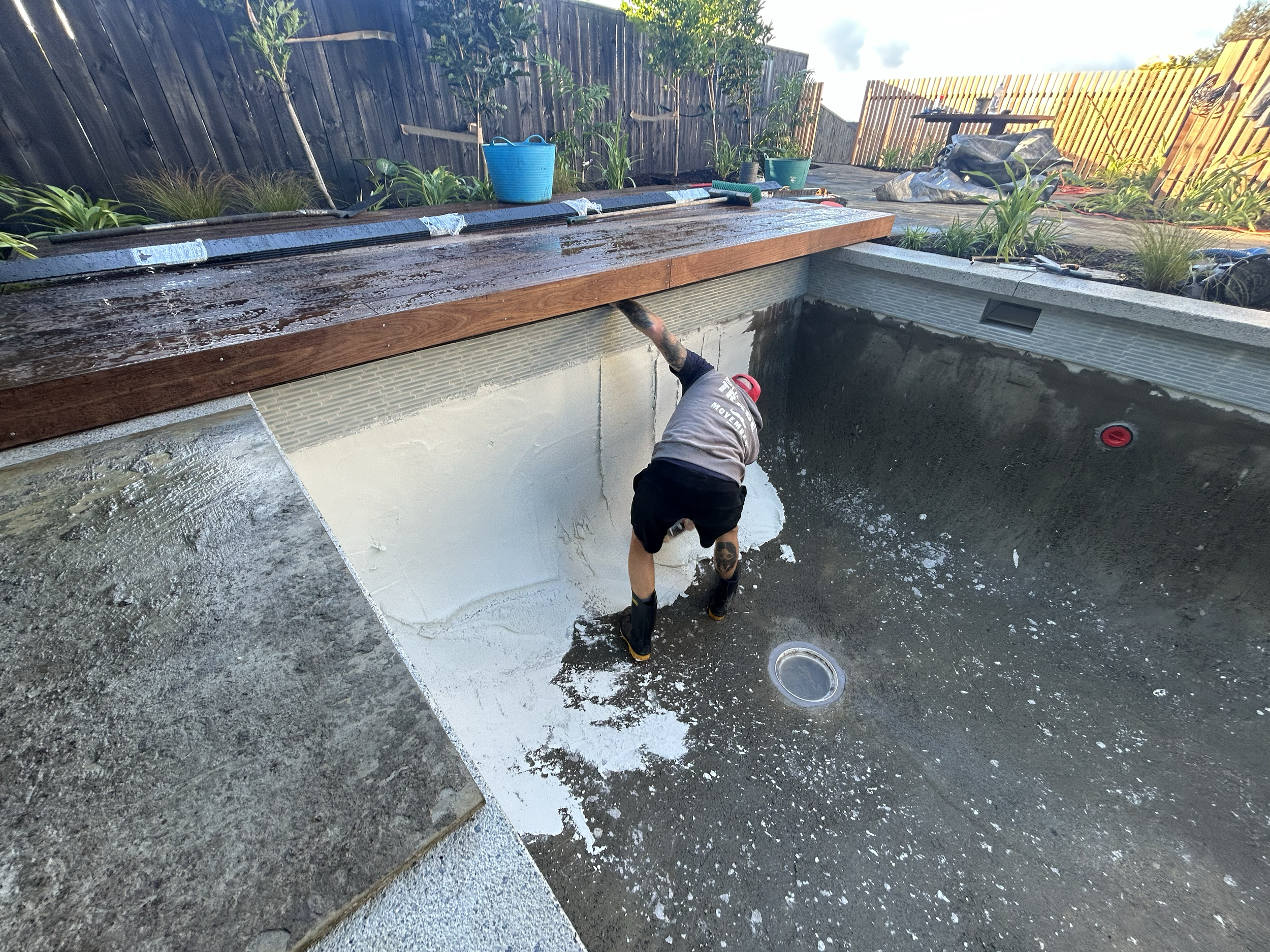 A person working on the construction of a swimming pool interior with some white plaster and a wooden deck is being installed at the edge of the pool. Existing pool refurbishment Built by ESC outdoor living swimming pool builders. Auckland. skilled