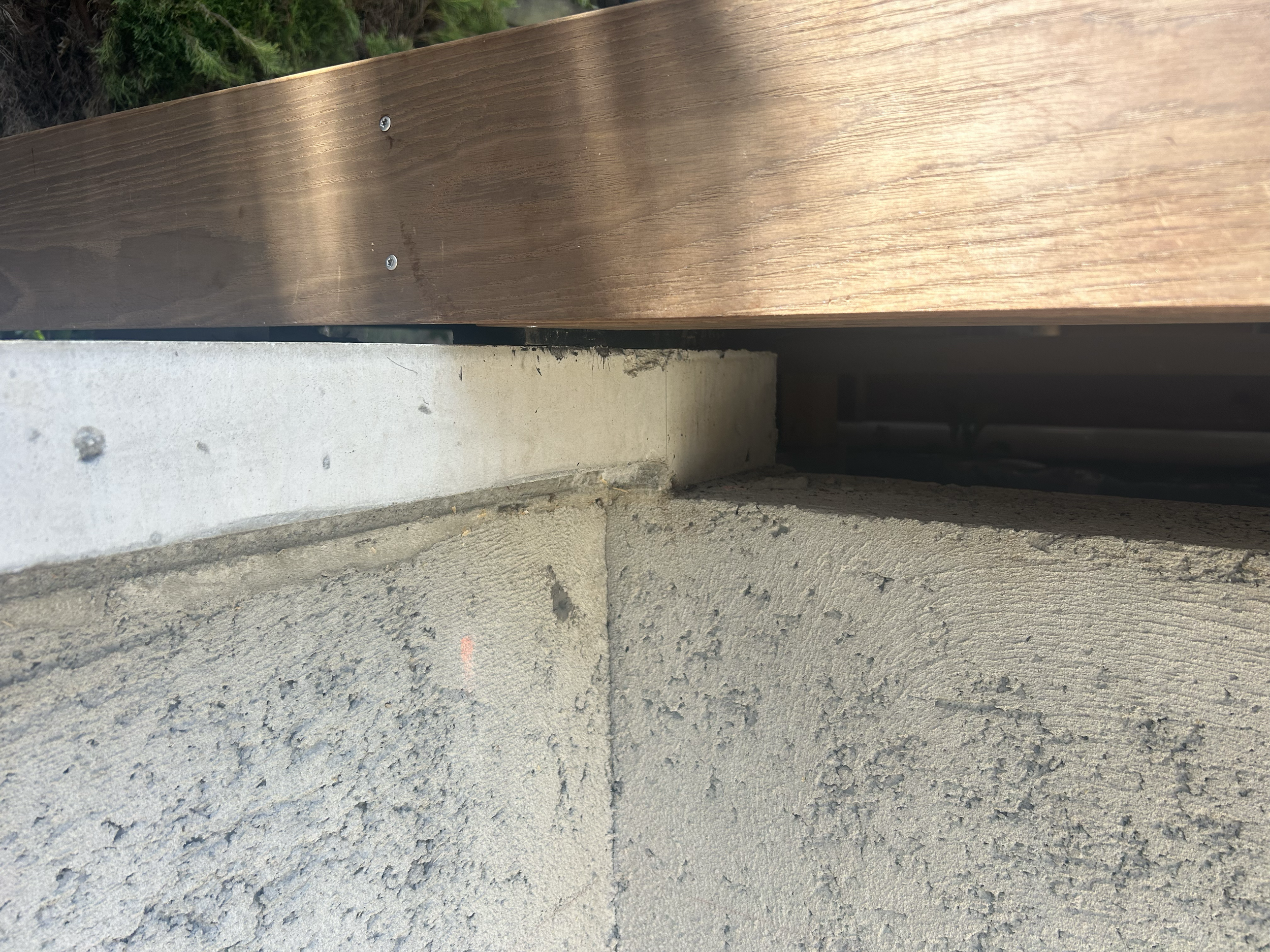 Close-up of a wooden handrail mounted on a gray concrete pool wall and a beige cinder block wall, taken from below. Existing pool refurbishment Built by ESC outdoor living swimming pool builders. Auckland. skilled builders