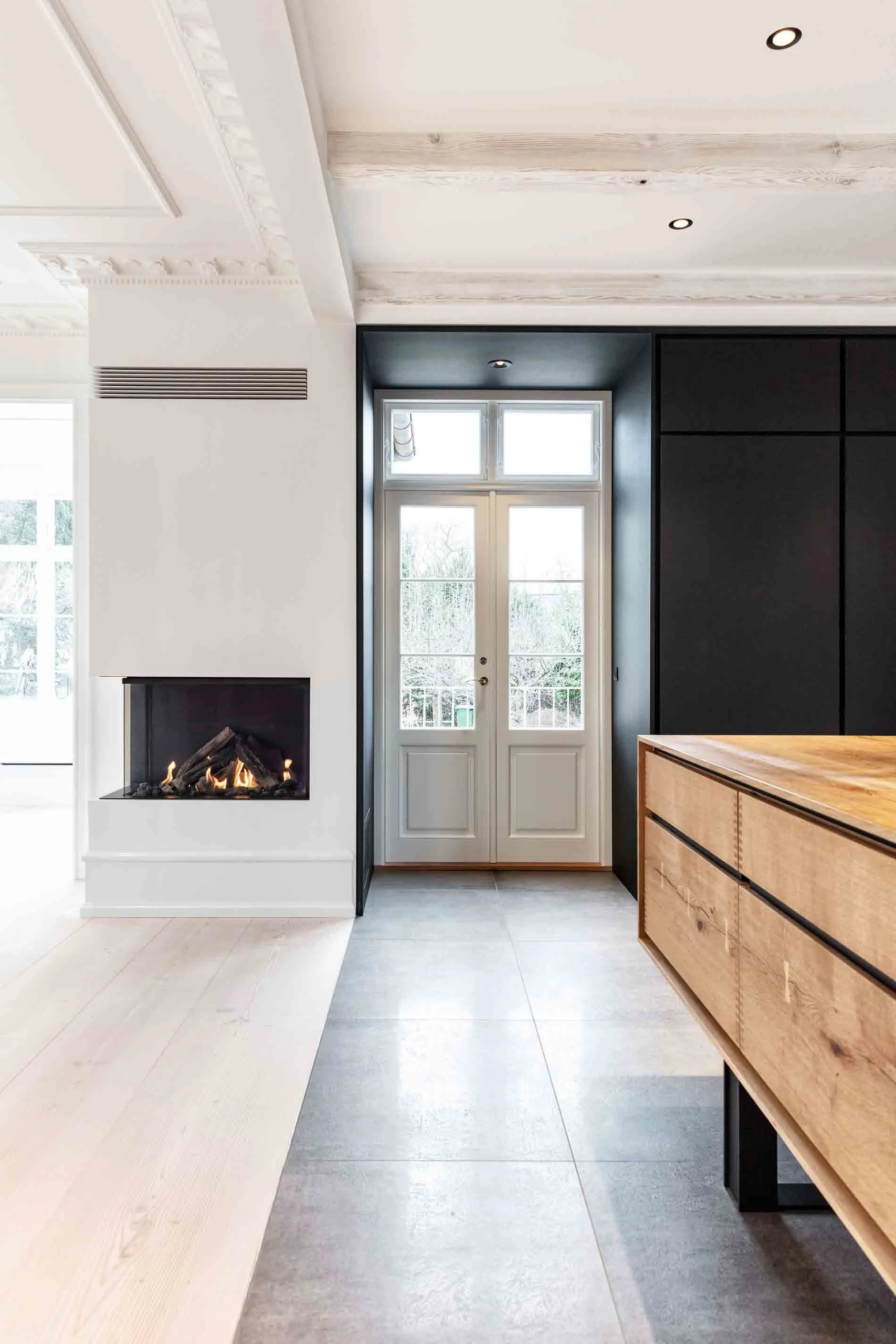 Indretning af et moderne hjem med en brændeovn, sort væg, hvid dør med vinduer, træskab og store gulvfliser.