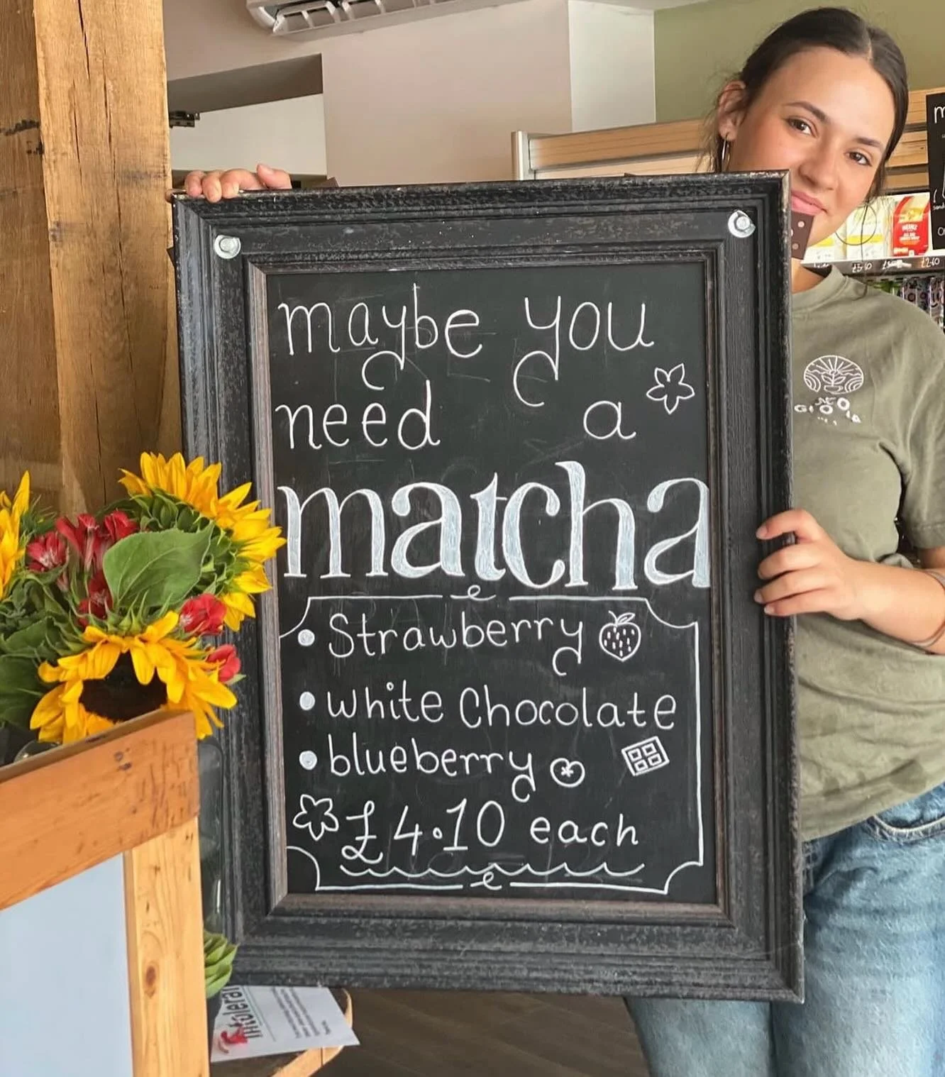 A barista holding up a blackboard with "Maybe you need a matcha?" written on it