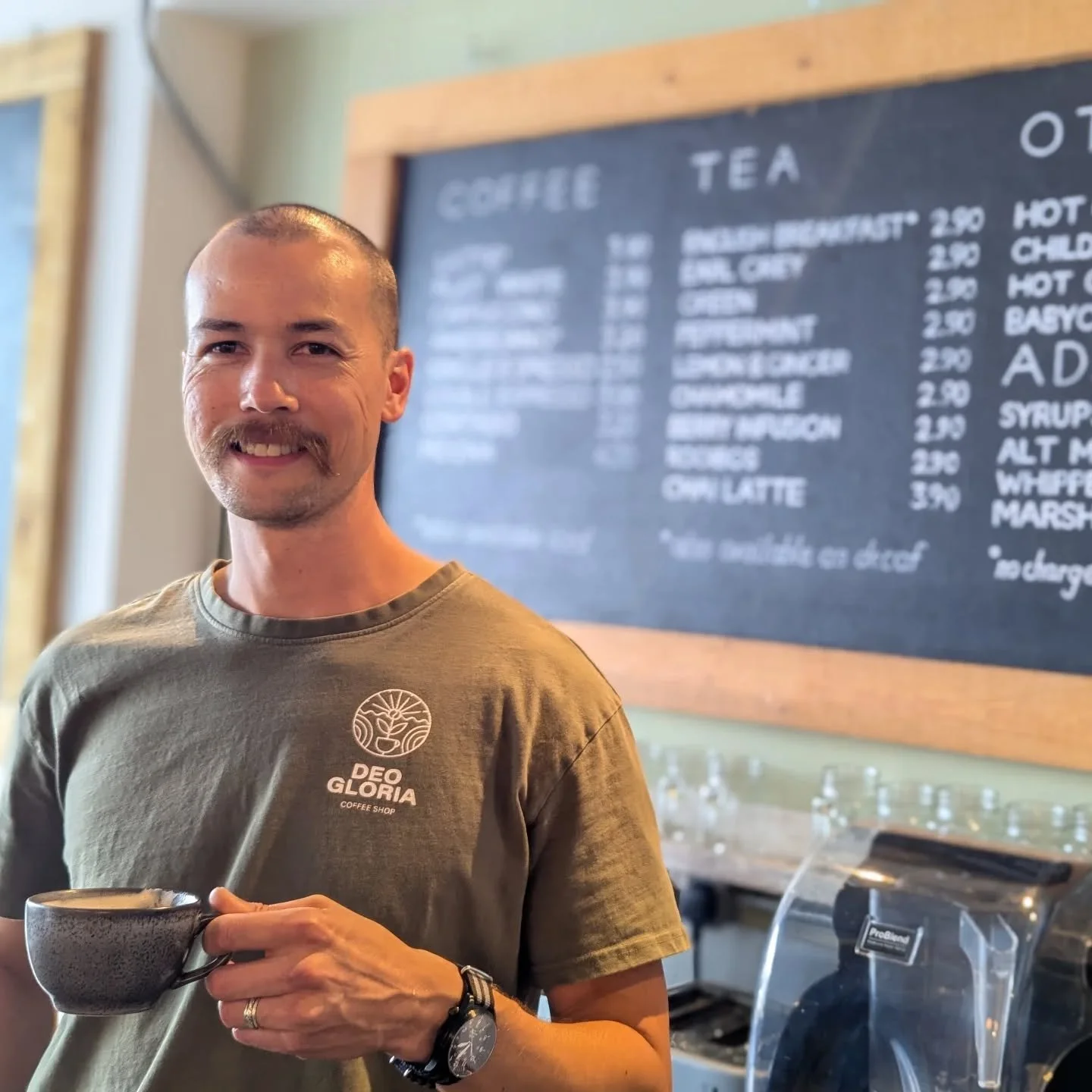 The Deo Gloria manager Matt smiling while holding a cup of his favourite Deo Gloria coffee