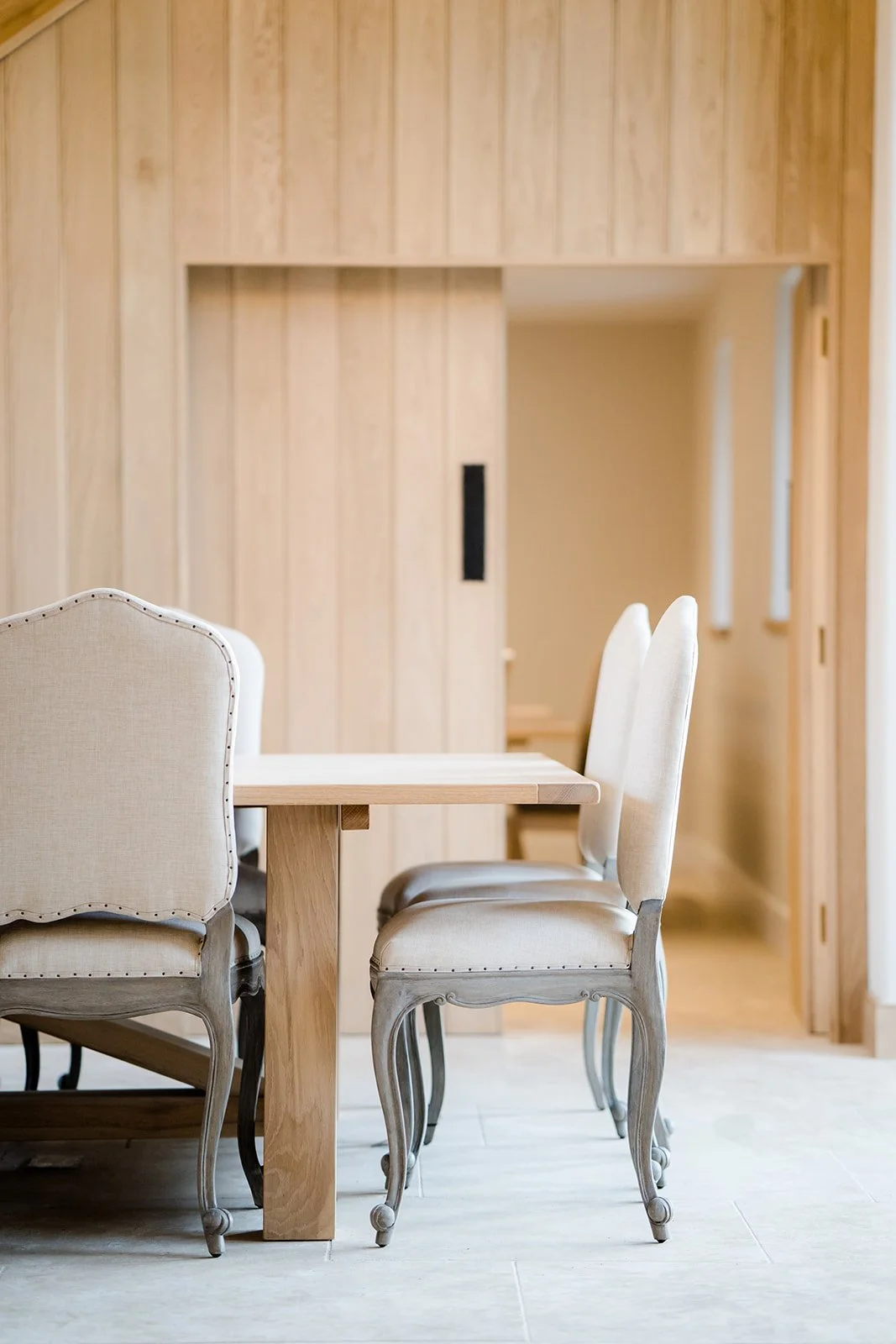 Dining room with cream upholstered chairs, wooden table, and wooden walls.
