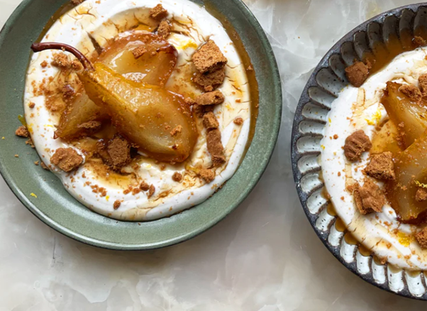 Pear dessert with whipped cream, crushed cookies, and caramel sauce in ceramic bowls.