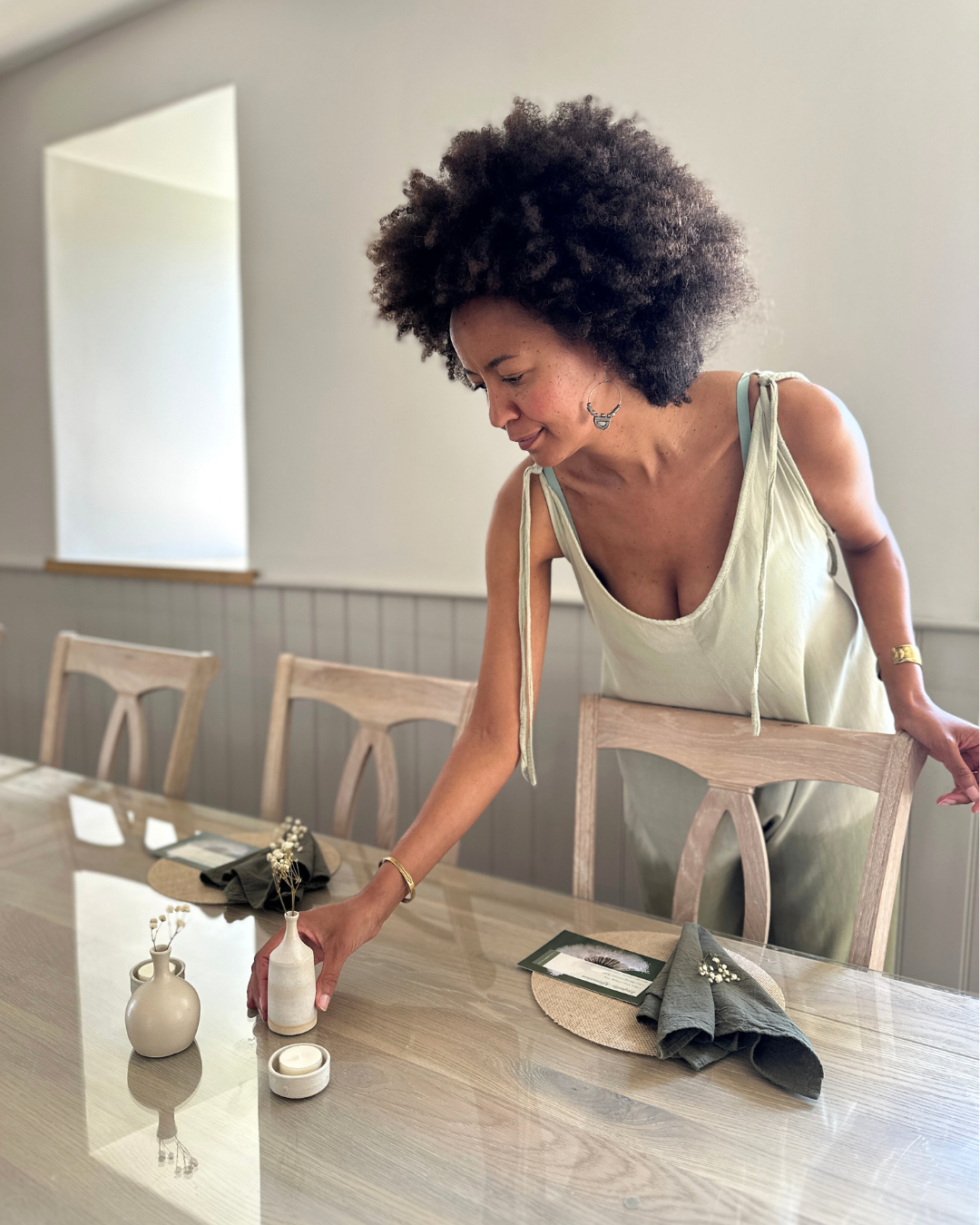 Woman arranging a small white vase with dried flowers on a wooden dining table. At a retreat in the cotswolds