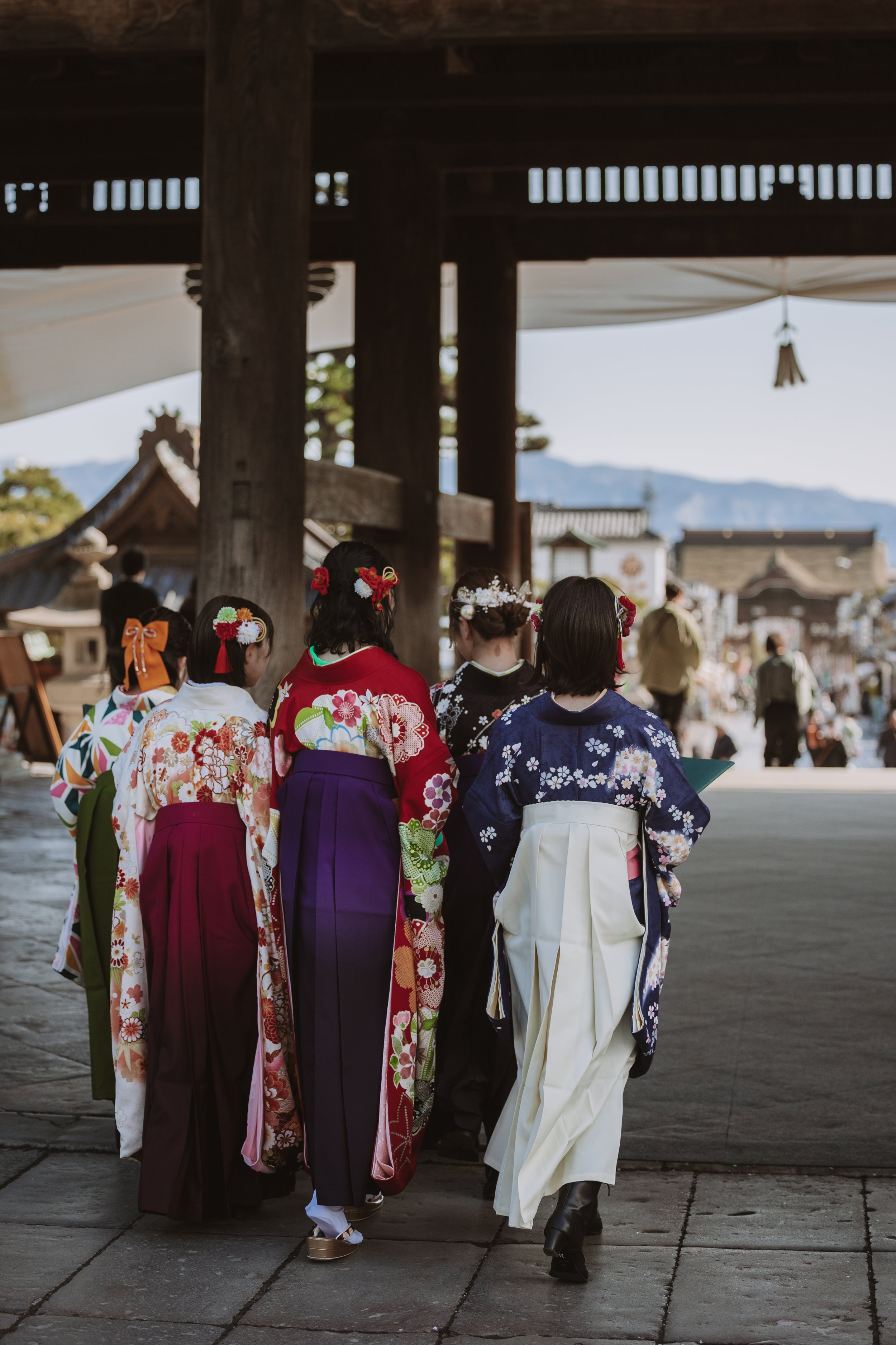 A group of women dressed in colorful traditional Japanese kimonos walking together in a shrine.