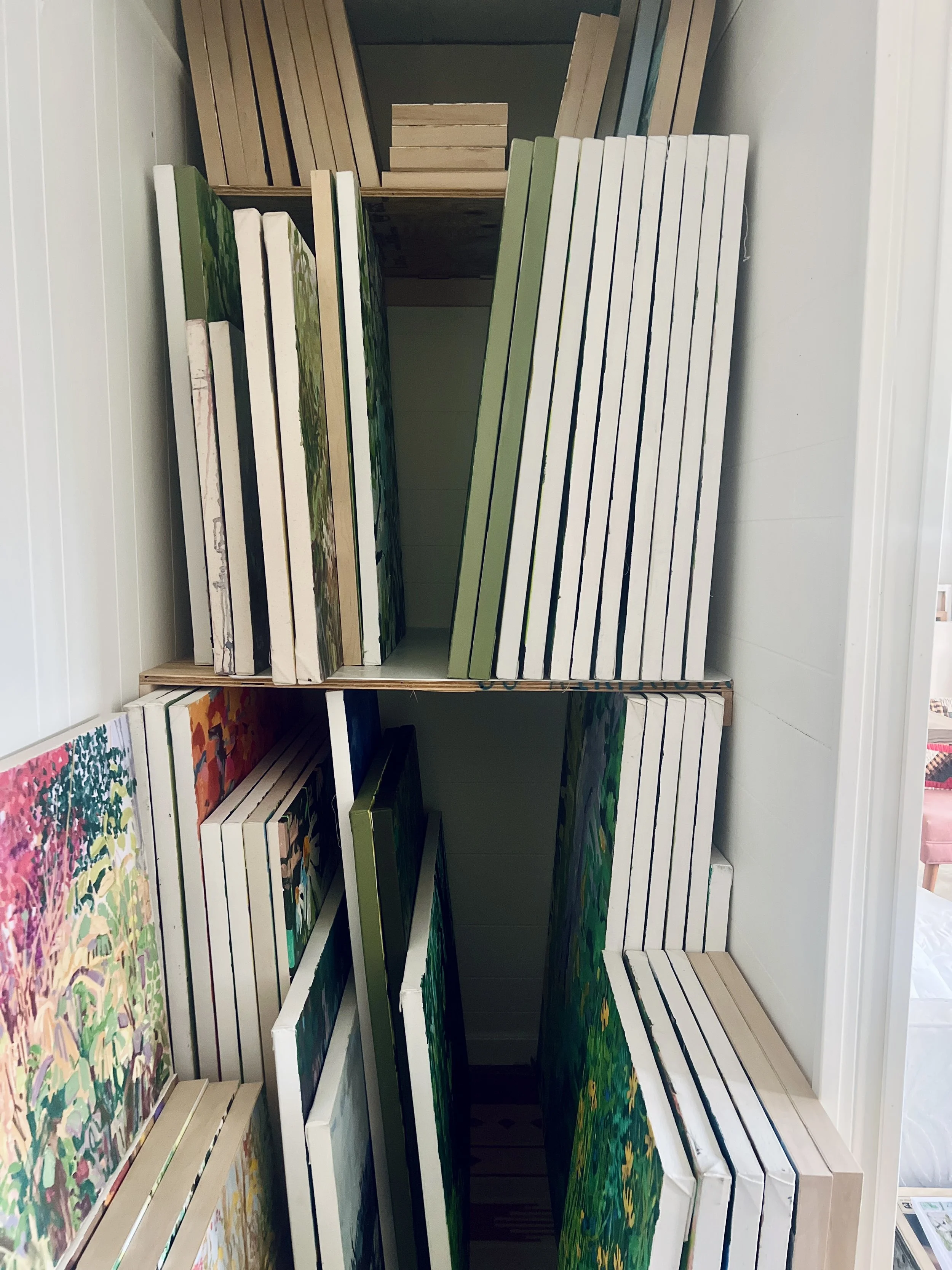 Paintings and art prints stored on shelves in an art supply store or gallery.