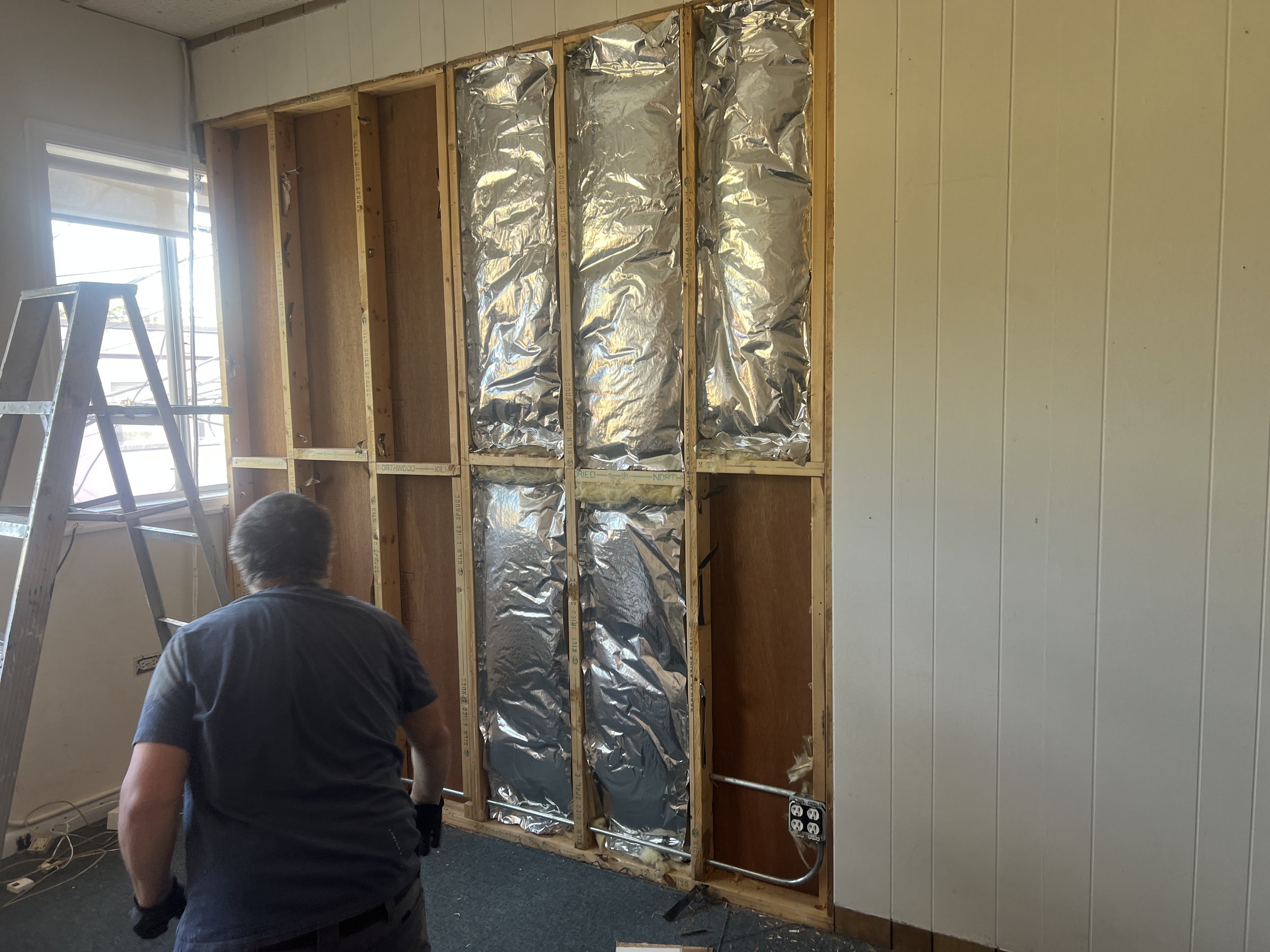 Vincent demolishing a wall frame in the studio with a window and electrical outlets.