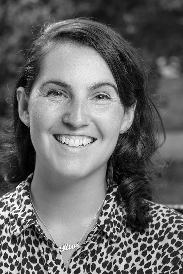 Black and white portrait of a woman smiling, wearing a leopard print blouse and a necklace with the name 'Gus' on it.