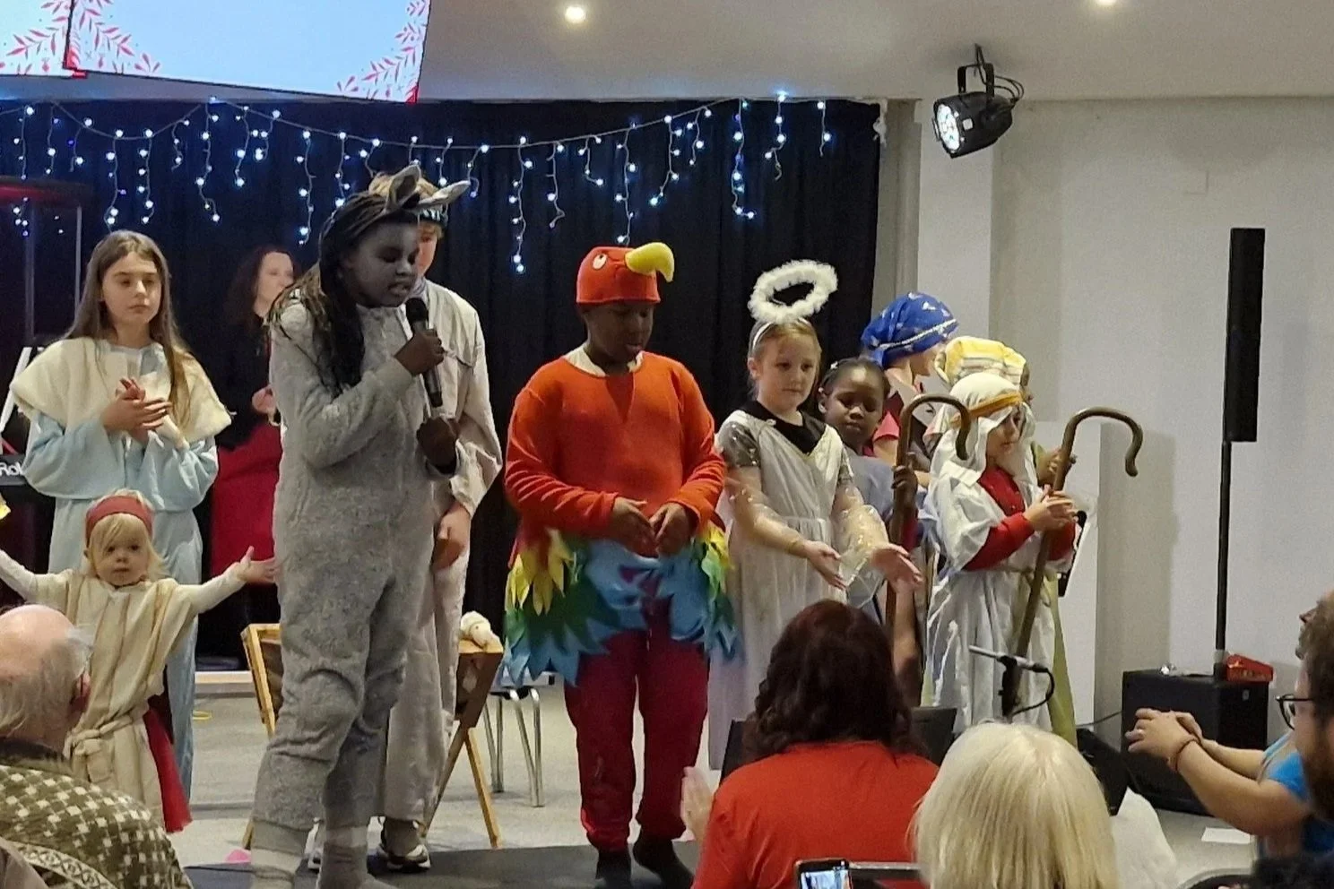 Children dressed in costumes performing a nativity scene on stage with an audience watching.