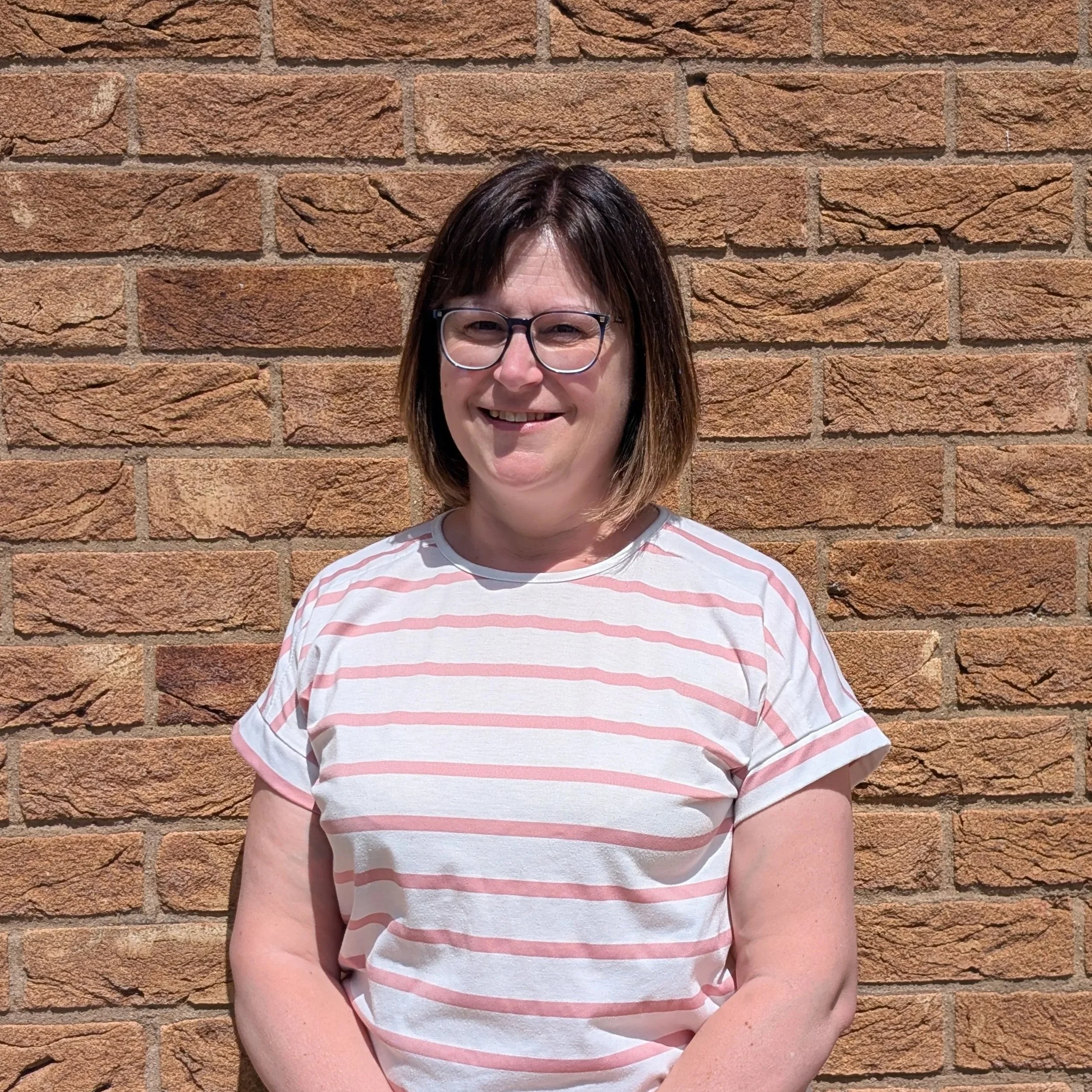 A lady smiling in front of a brick wall.