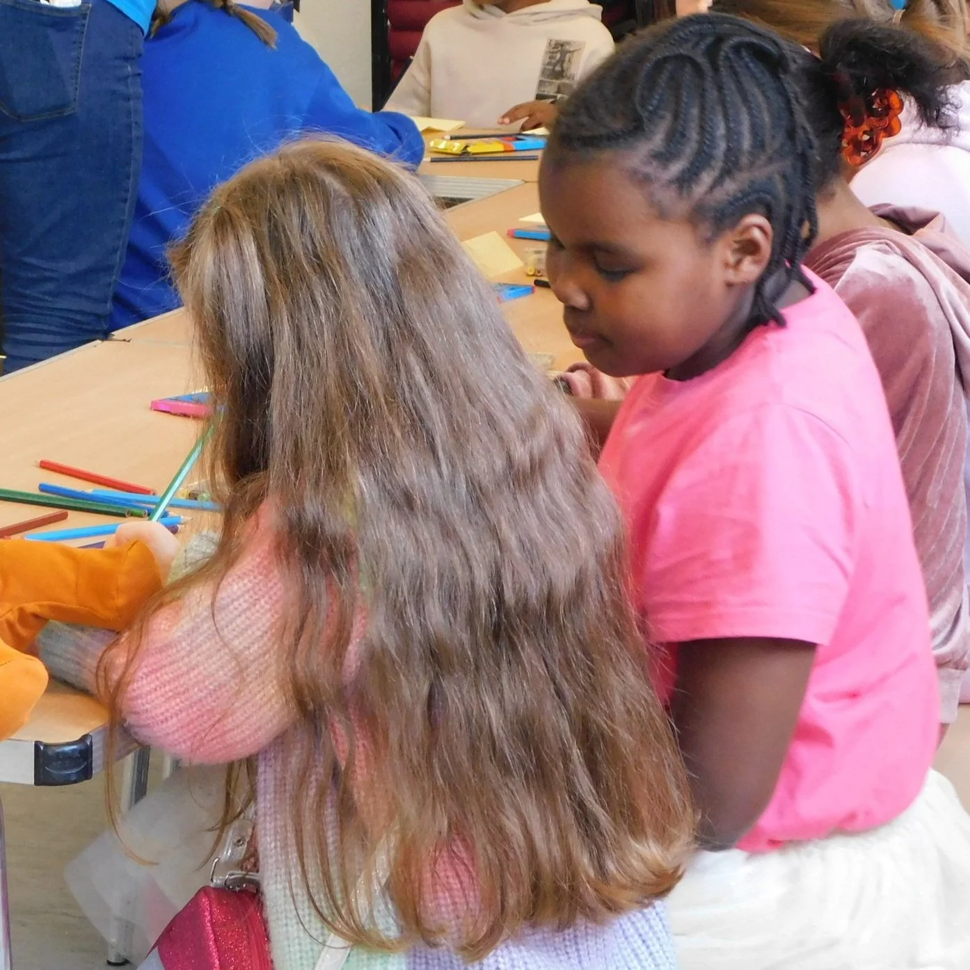 Children gathered around a table working on colorful colored pencils and papers in a classroom setting.