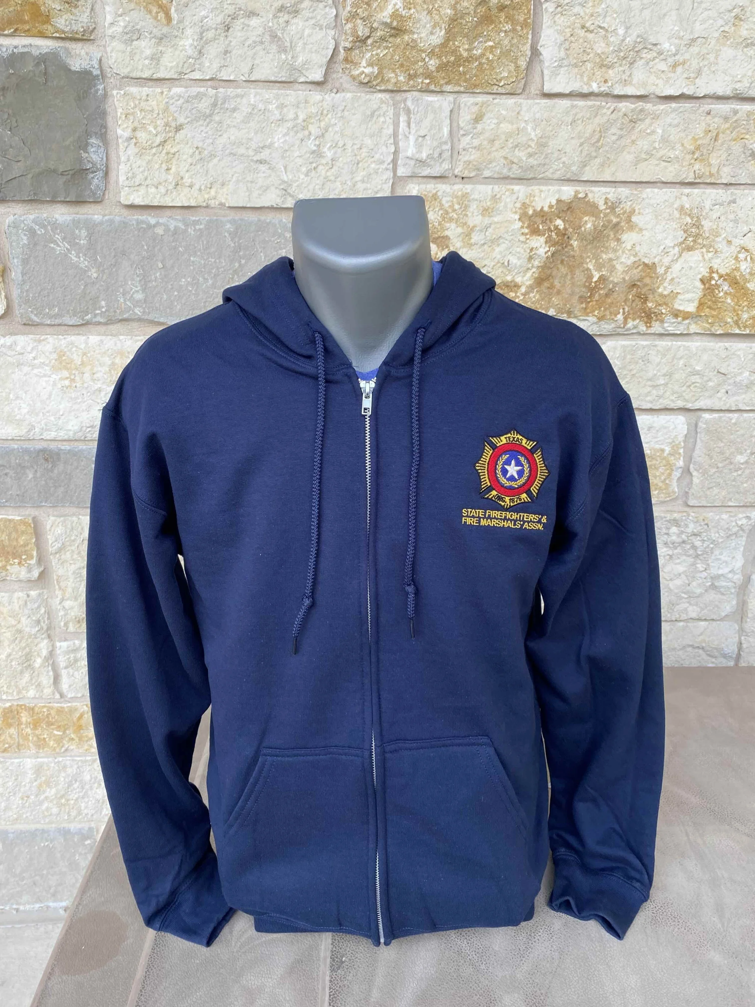 A person wearing a gray hat with red embroidered letters, 'SFFMA', and a black-and-white patterned shirt, outdoors with blurred background.