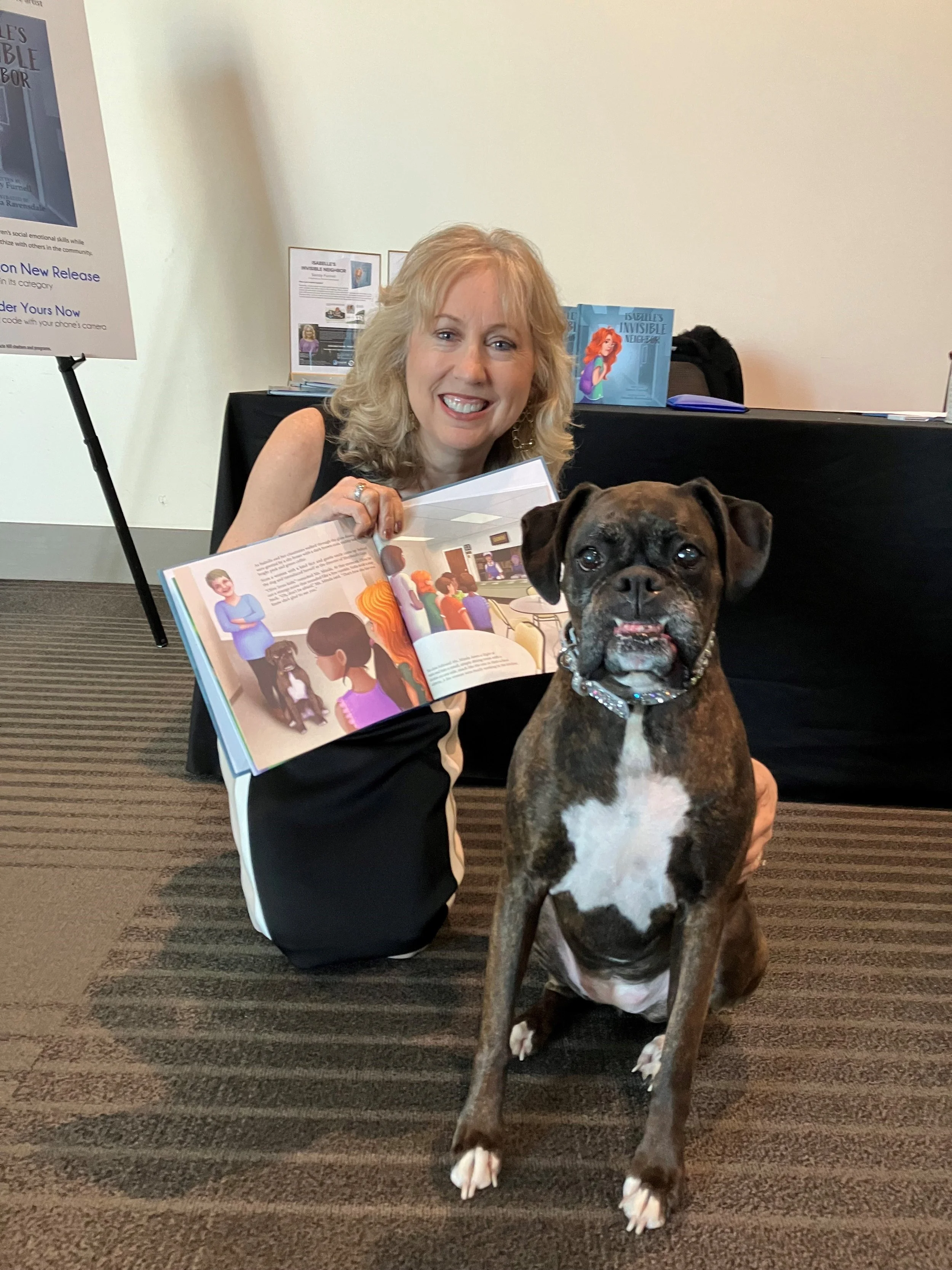Sandy Furnell holding Isabelle's Invisible Neighbor book next to brown boxer dog, Olive