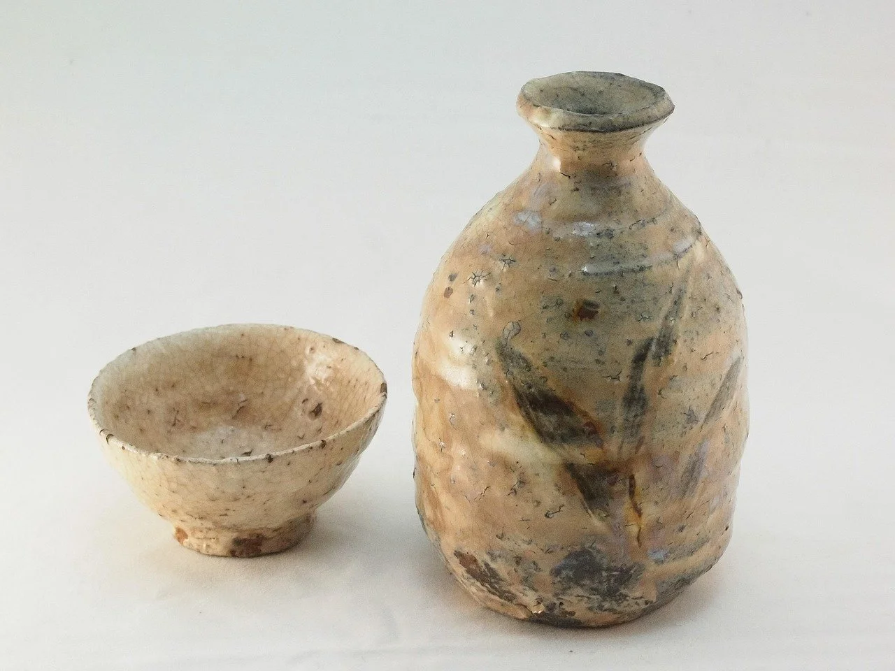 Ancient pottery for pouring and drinking sake, consisting of a small bowl and a larger sake vessel with faded glaze and irregular surface.