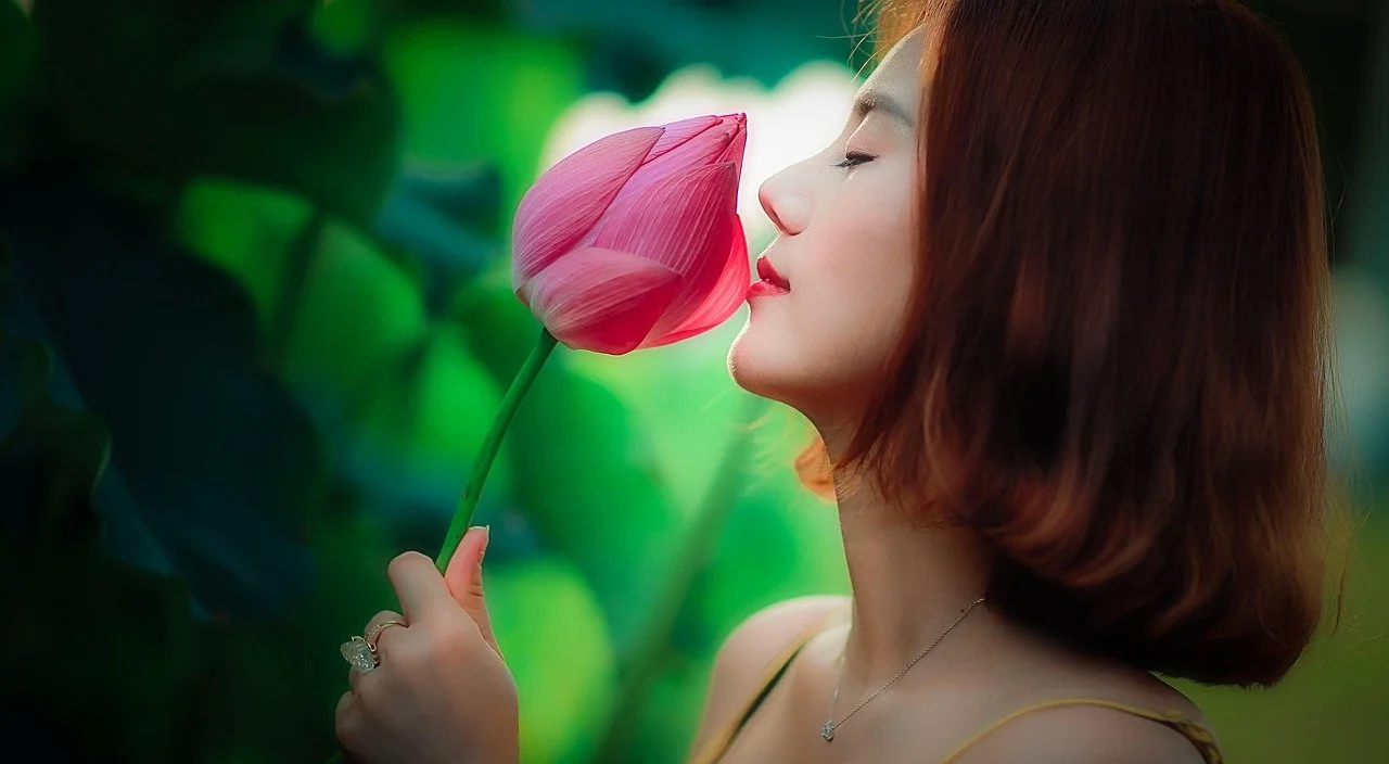 A woman with auburn hair holding a pink tulip close to her face.