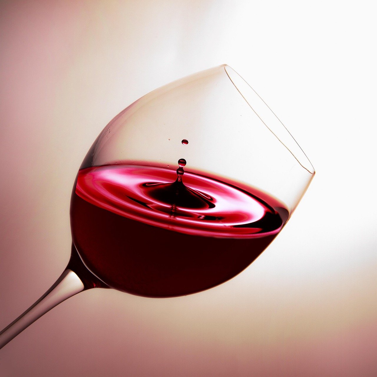 A glass of red wine tilted with a droplet falling into it, creating ripples in the wine.