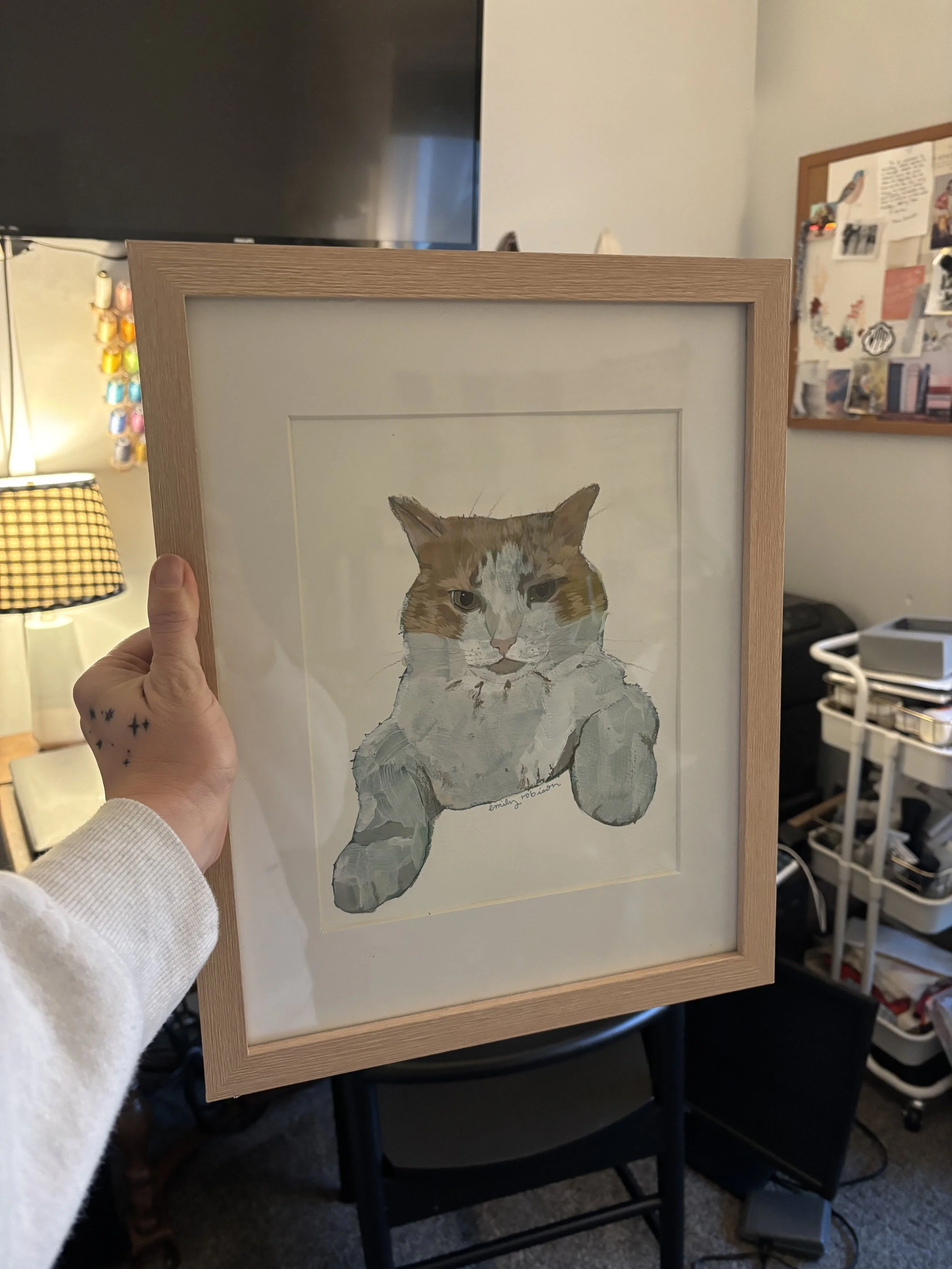 Picture of a hand holding up a framed original pet portrait painting of an orange and white cat done in an impressionistic style using gouache paint and colored pencils on coldpress watercolor paper.