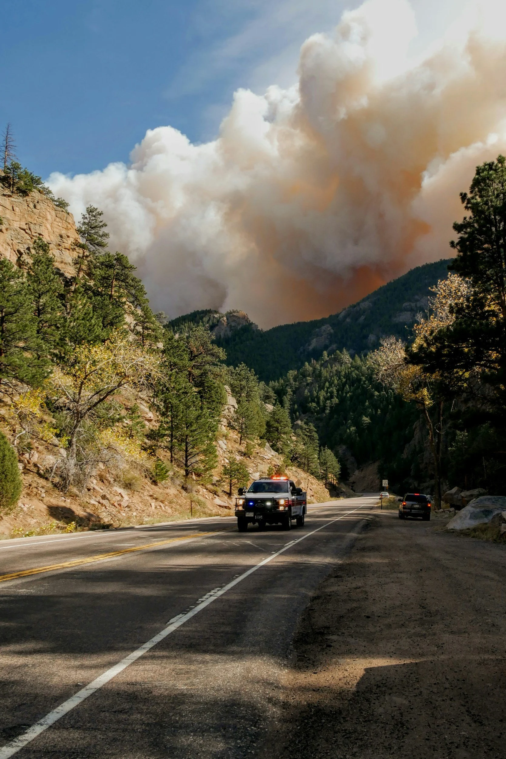 Wildfire smoke over a mountain road with a police vehicle.