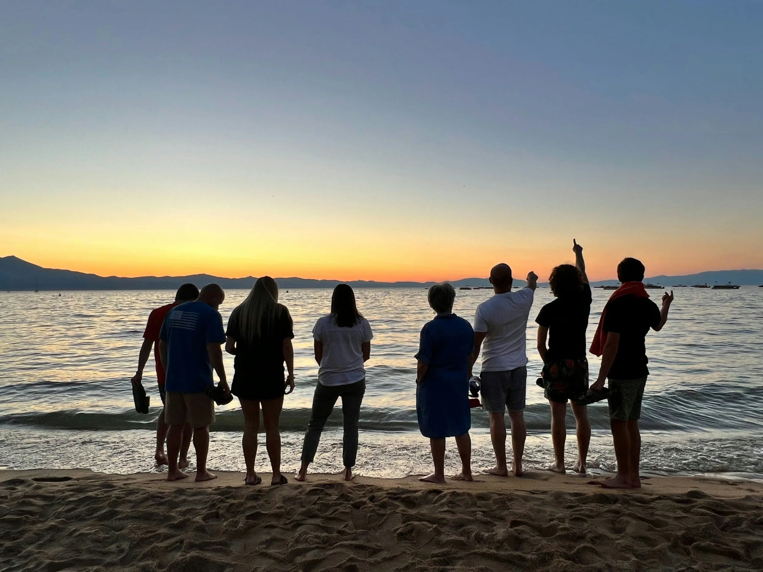 People standing on a beach facing the ocean at sunset