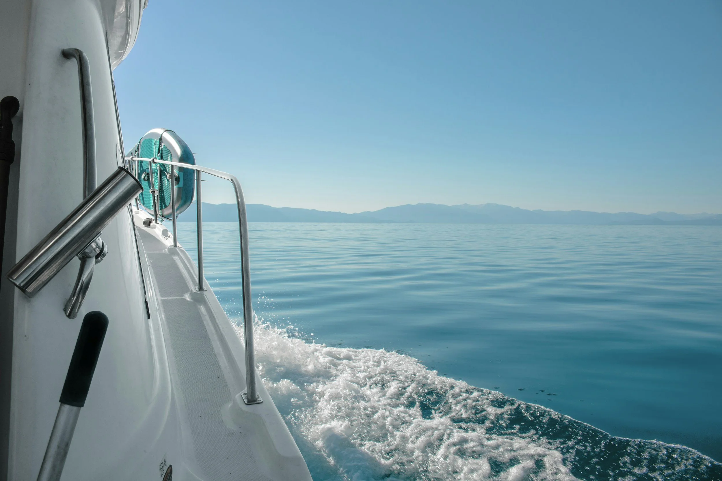 View from a boat looking over calm blue water with a distant mountain range on the horizon under a clear sky.