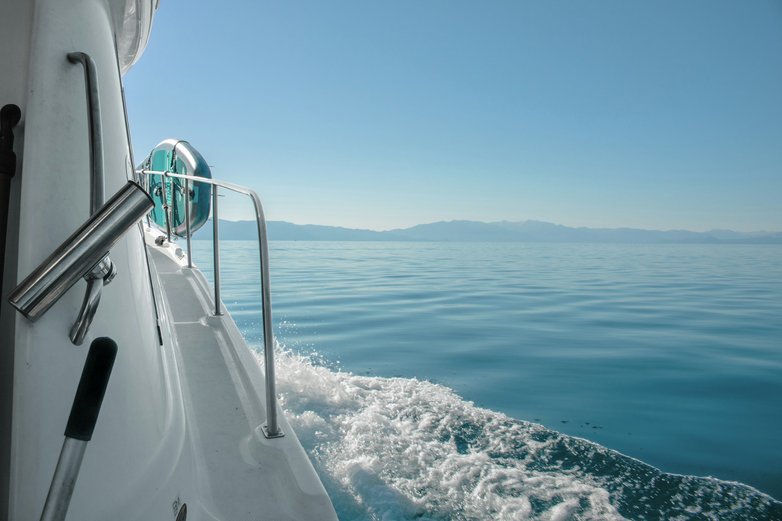 View from a boat looking over calm blue water with a distant mountain range on the horizon under a clear sky.