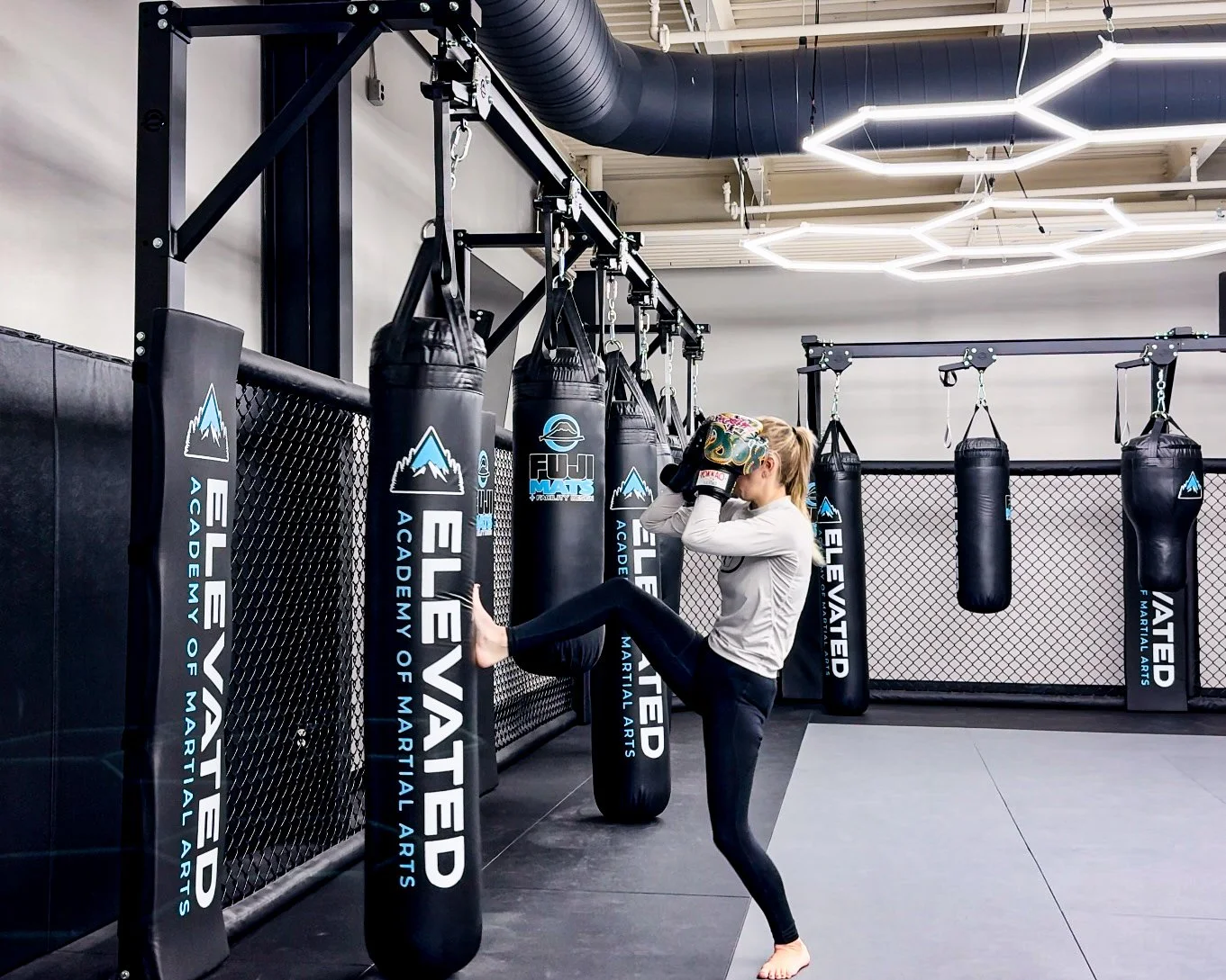Woman practicing karate kick on punching bag in martial arts gym.