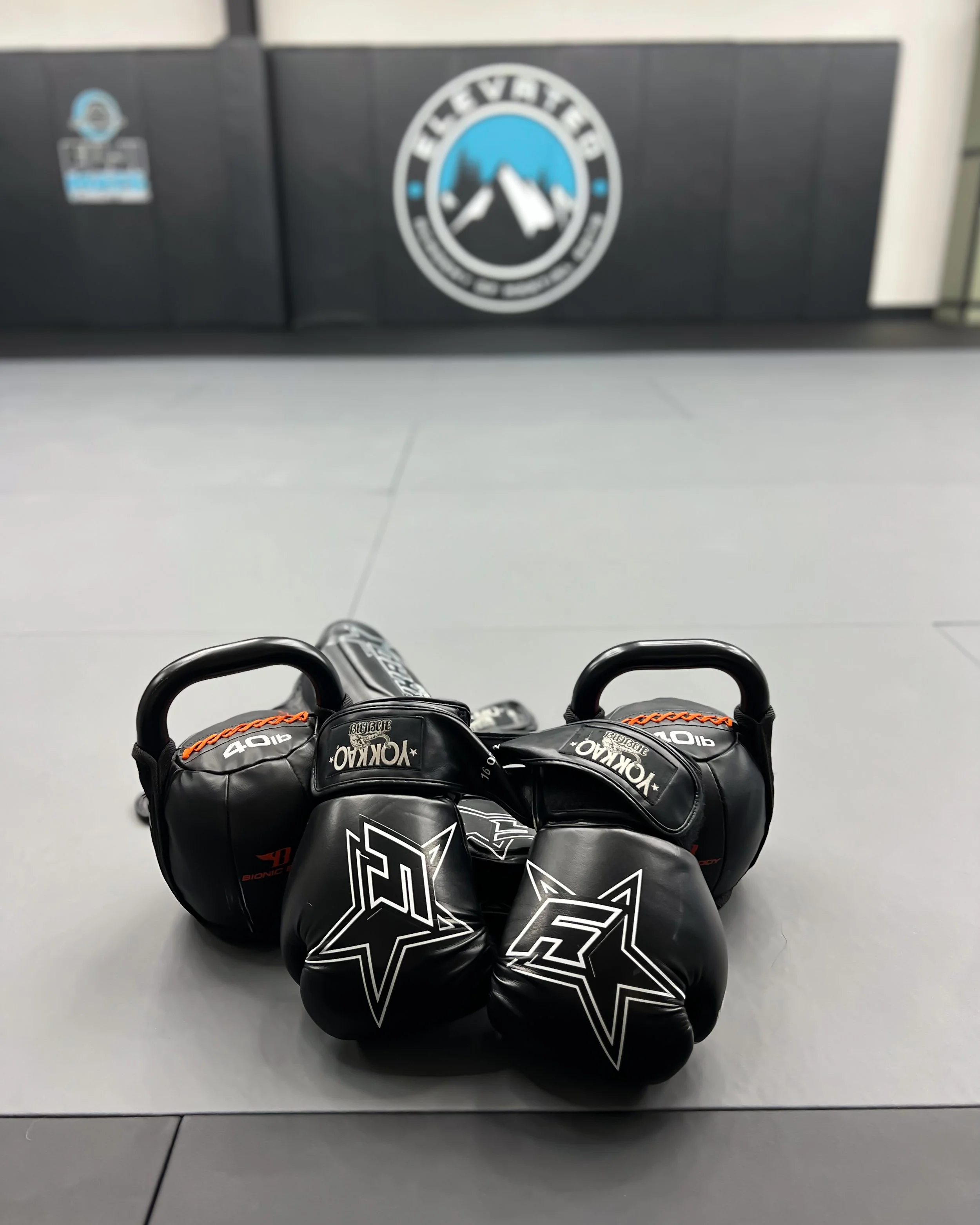 Boxing gloves and kettlebells on a gym mat with logo in background.