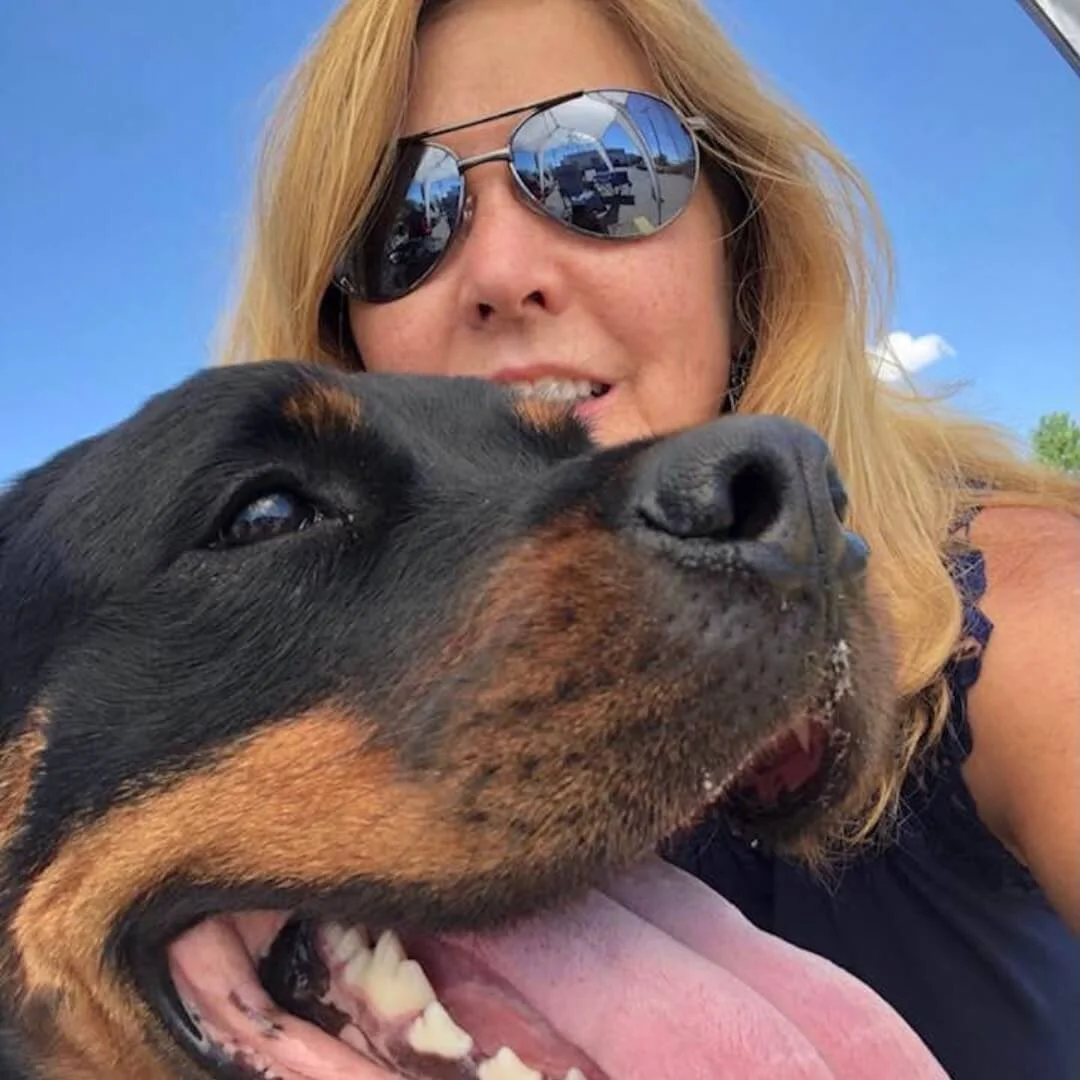 Deborah Rohan wearing sunglasses and posing with a large Rottweiler dog
