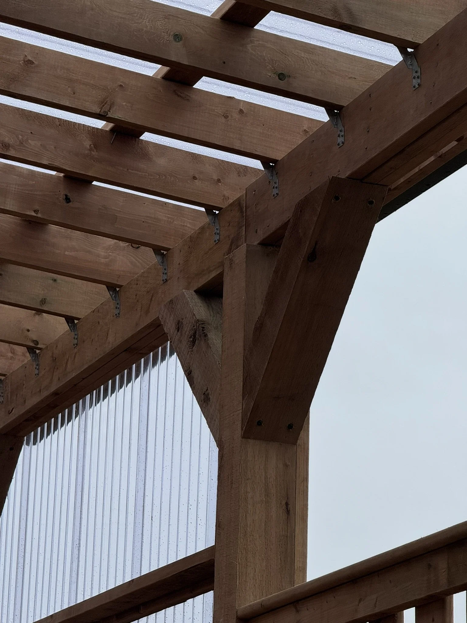 Close-up view of a wooden roof frame with metal brackets, viewed from below against the sky.