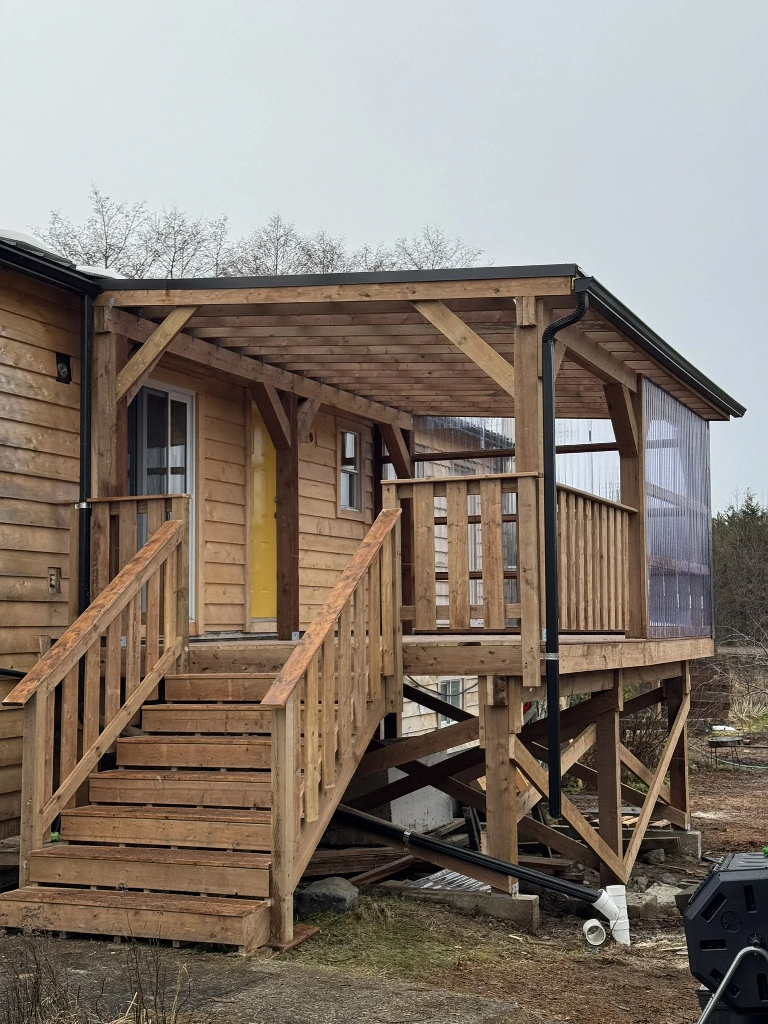 A wooden deck under construction attached to a house, with stairs leading up and supported by wooden posts and beams.