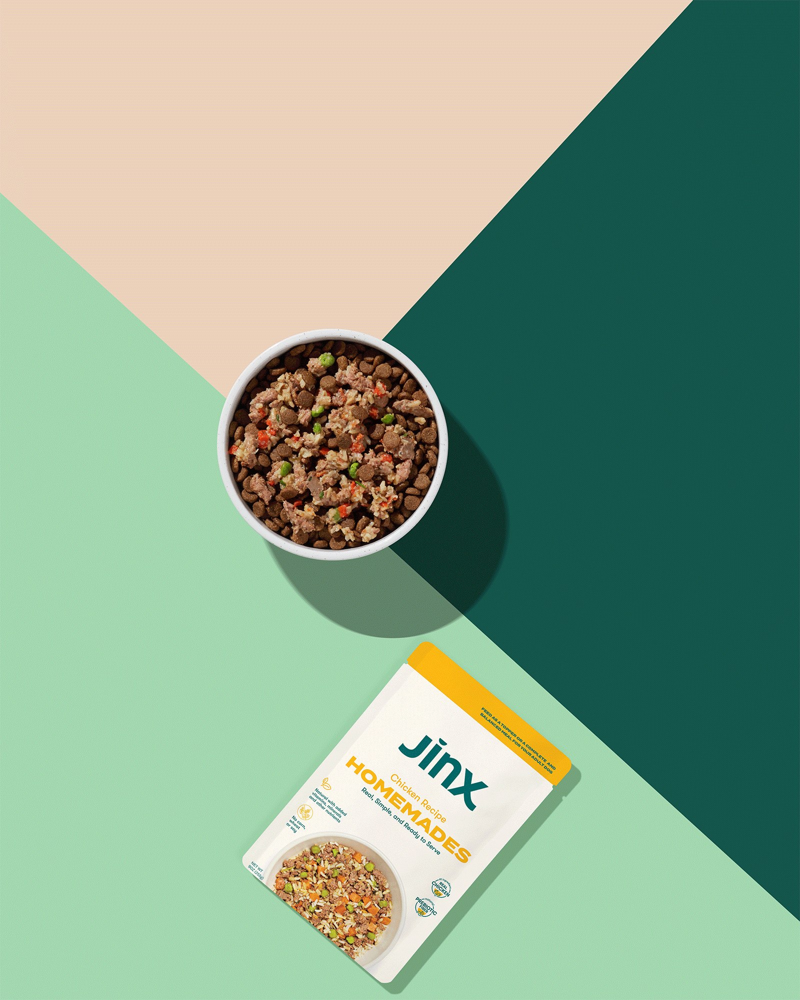 A bowl of dog food with kibble and mixed ingredients, and a Jinx brand homemades chicken recipe food package against a colorful geometric background.