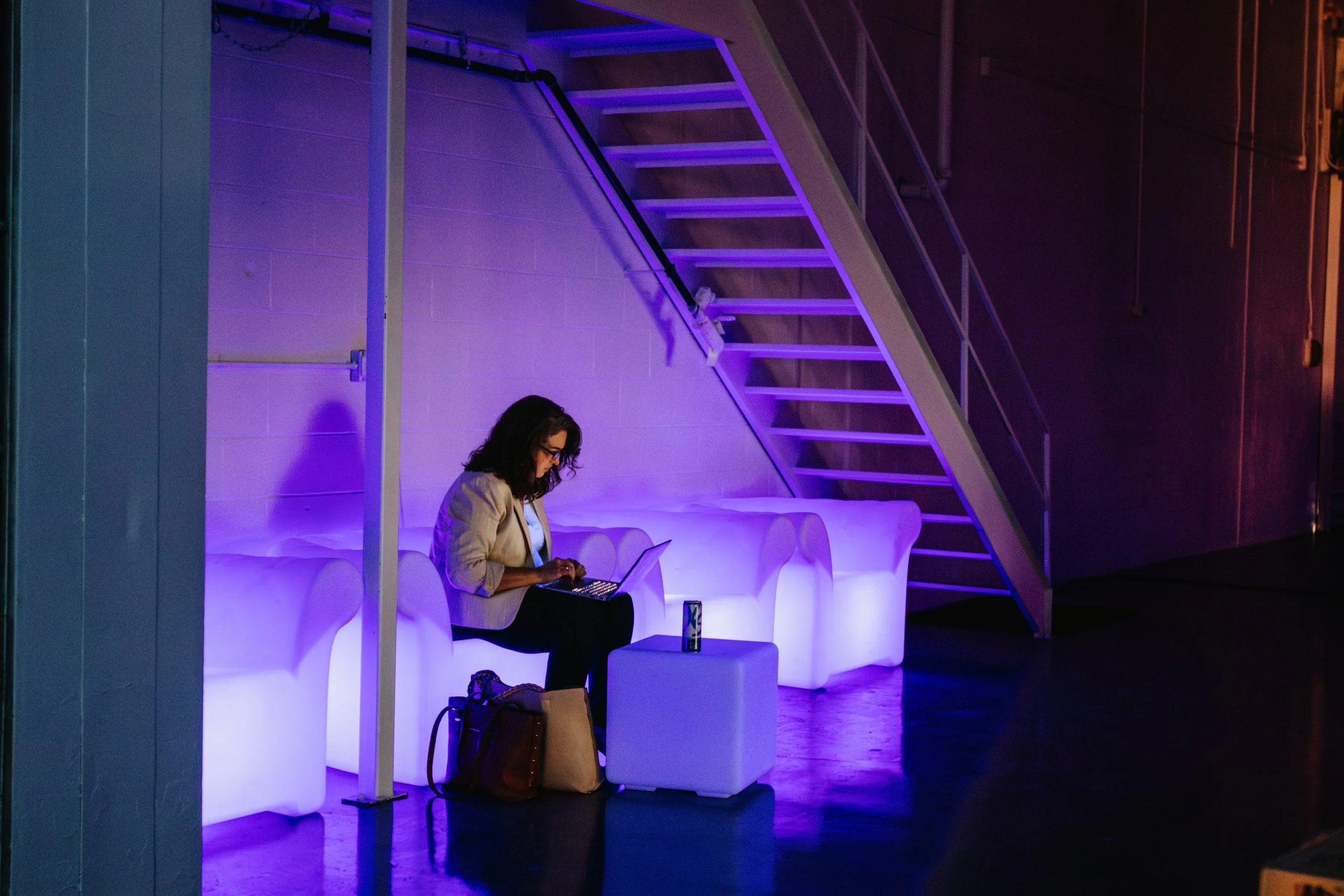 Woman sitting on a couch working on her computer at Golden Hour studio with purple LED lighting.