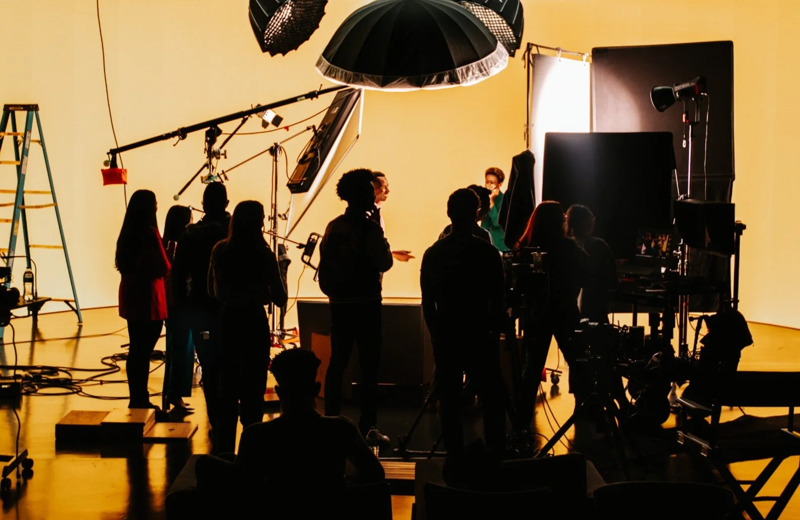 Behind-the-scenes photo of IDEOLOGY's Golden Hour studio with crew members and production equipment on set, illuminated by warm yellow light across the screen and background.
